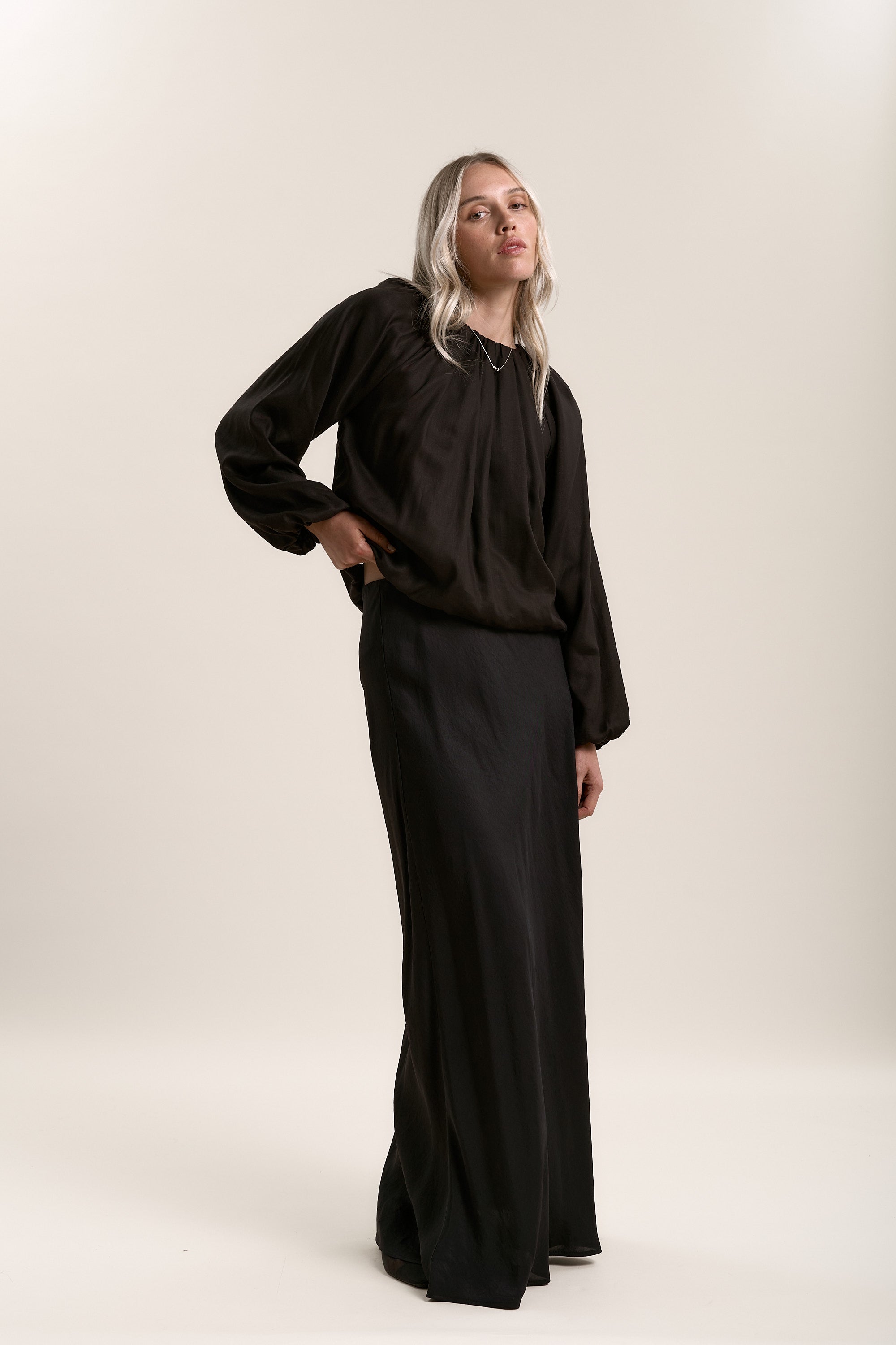 Woman with blonde hair wears Max's Lee Gathered Top and a long black skirt on beige background.