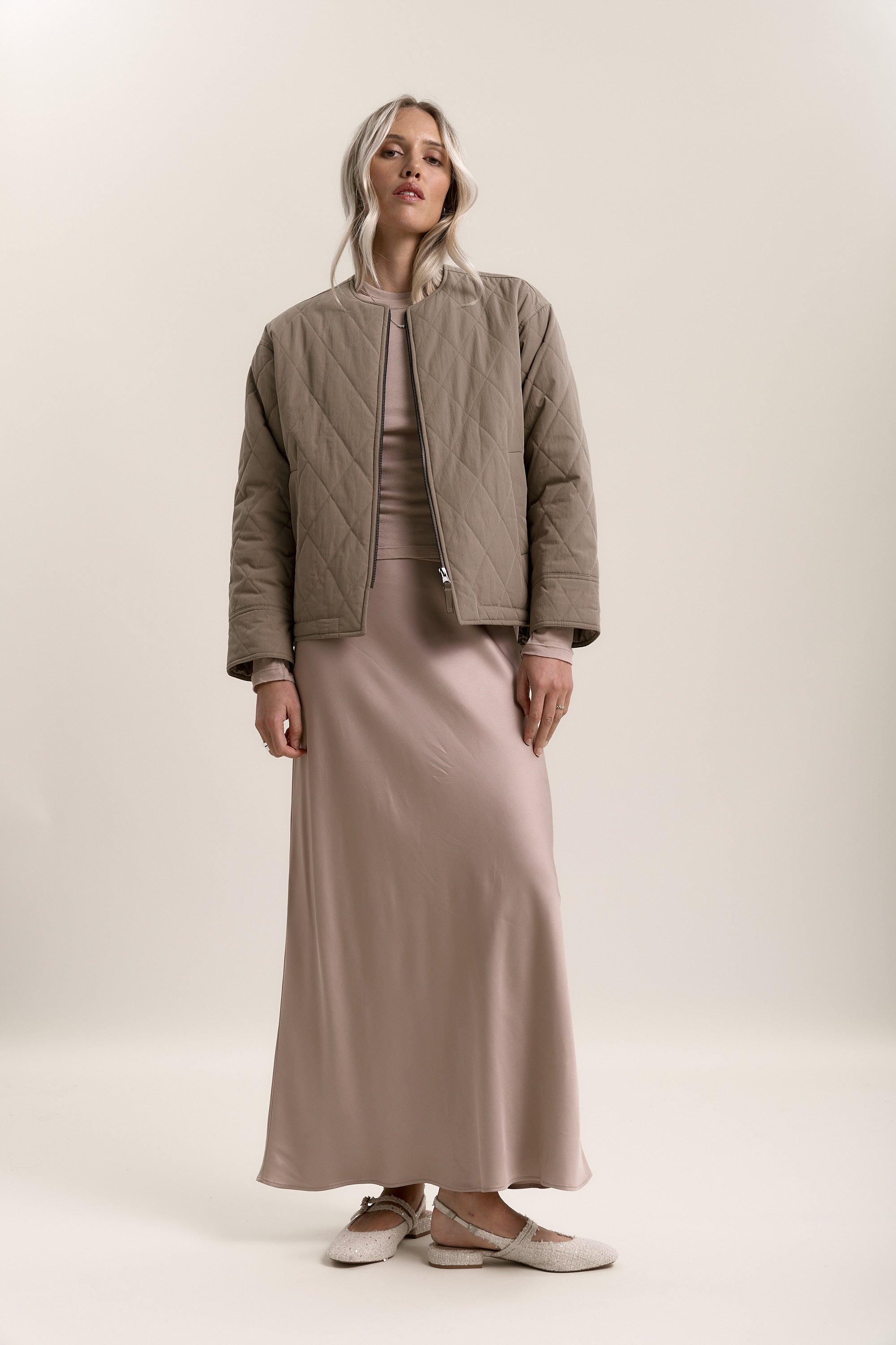 Woman in a beige quilted jacket and Max Holly Slip Skirt, standing against a plain background.