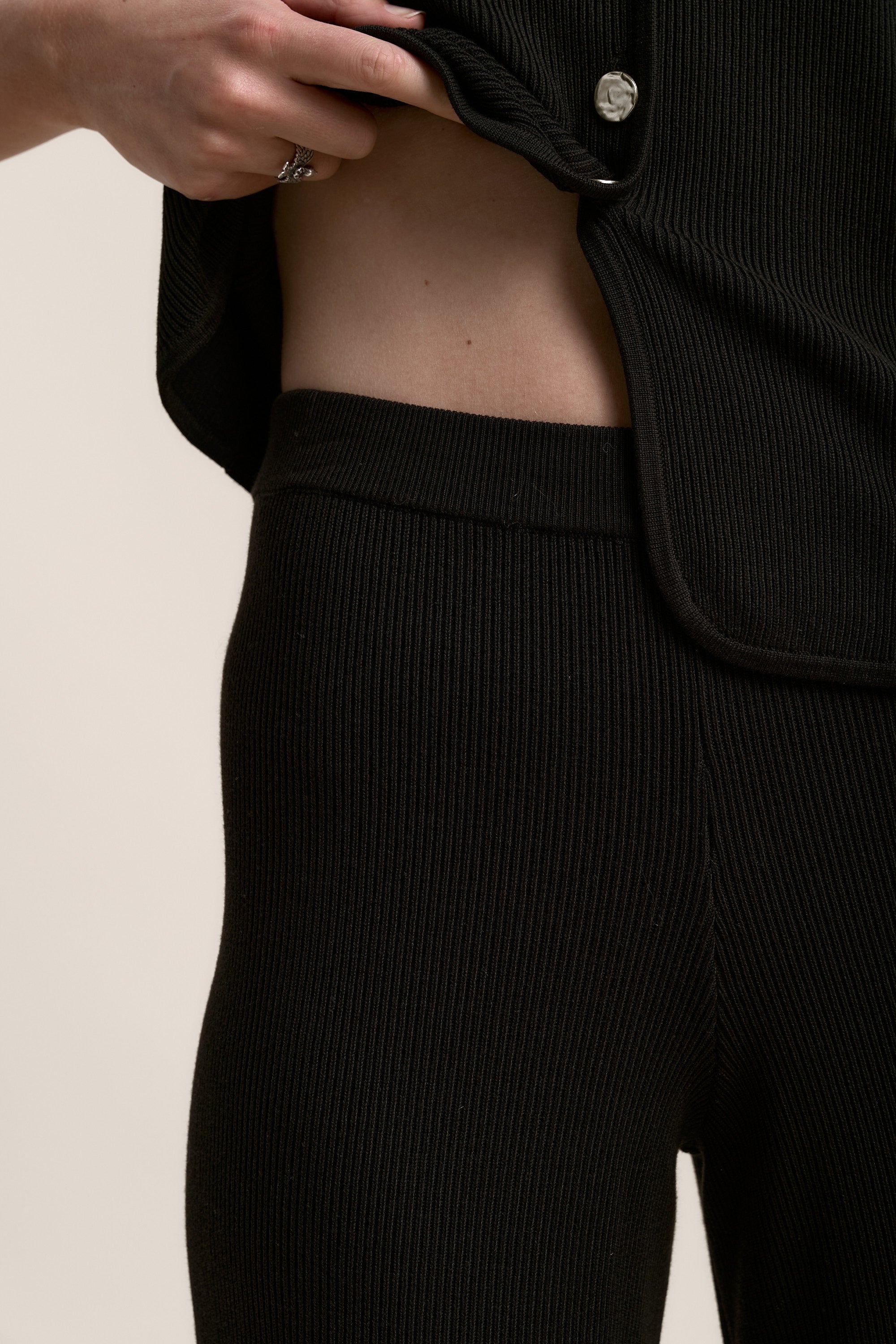 Person wearing Max Charlie Knitted Pants in black, lifting shirt to show waist.