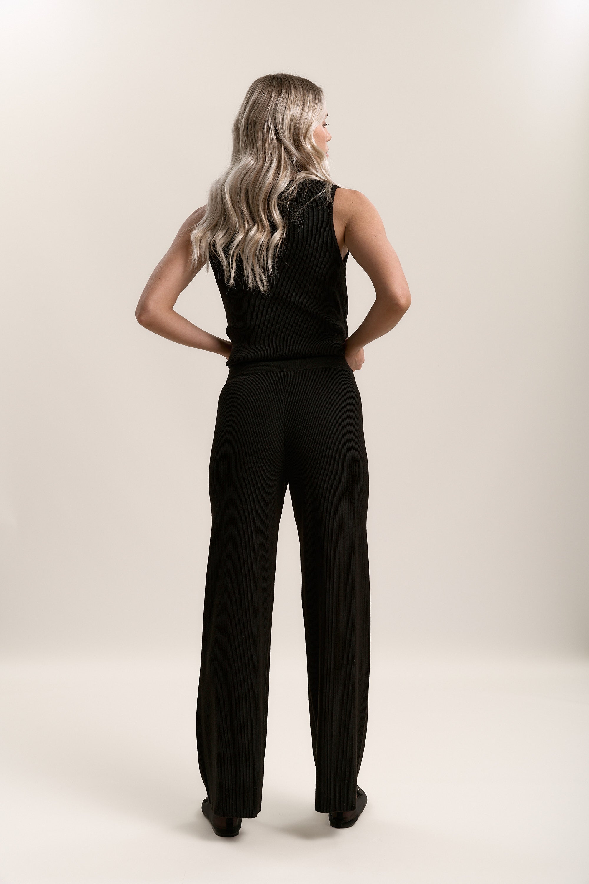 A woman with long blonde hair wears Max’s Charlie Knitted Pants in black, high rise, wide leg.