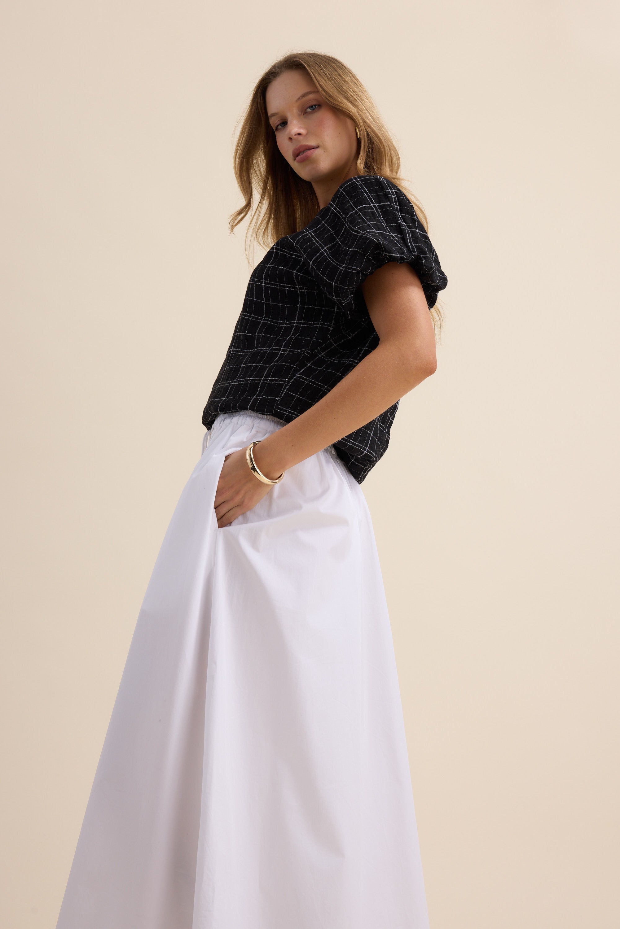 Max's The Bubble Hem Top in black checks, styled with a white skirt and hand in pocket.