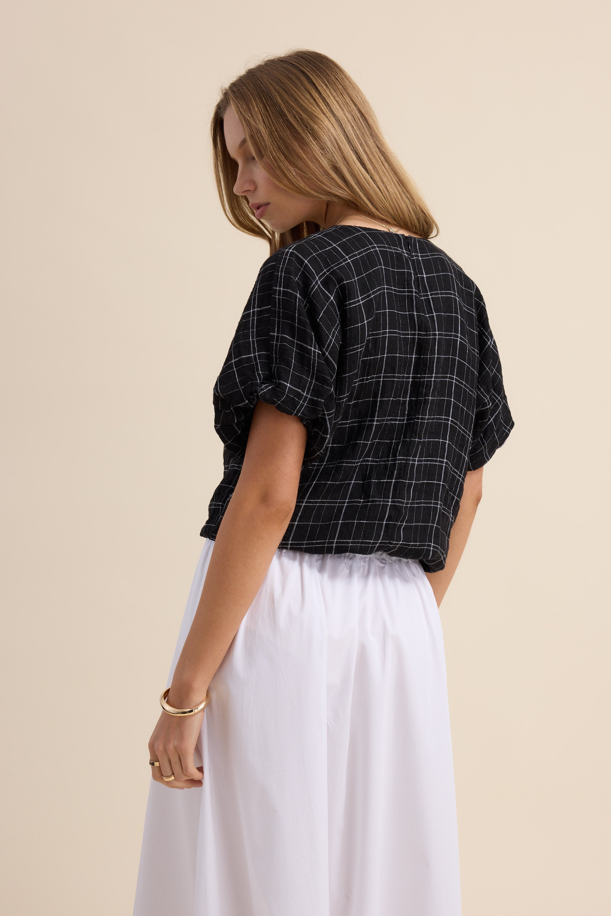 Woman in Max’s The Bubble Hem Top, a cropped blouse with black checks, and white skirt.