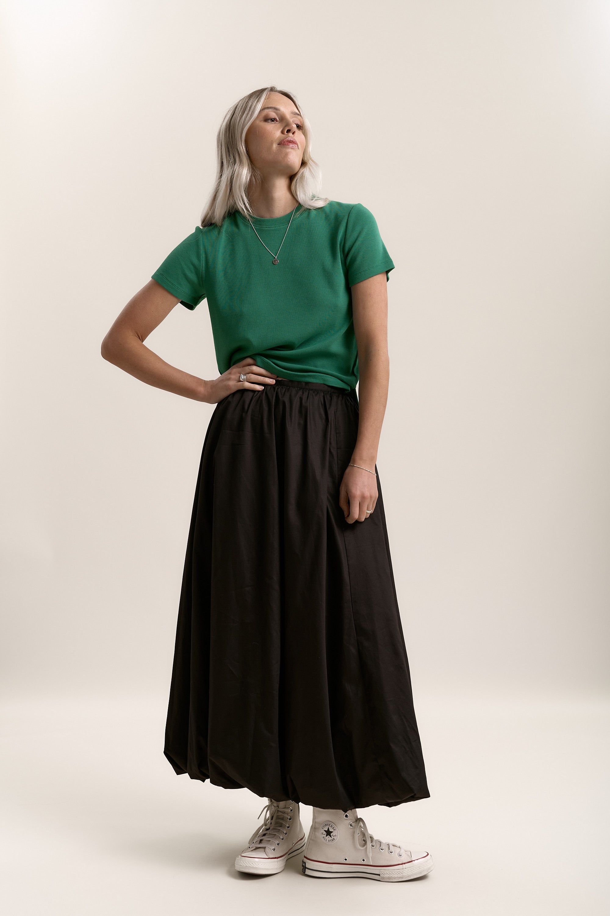 Woman in green shirt and Max's Juniper Bubble Hem Skirt with white sneakers against plain background.
