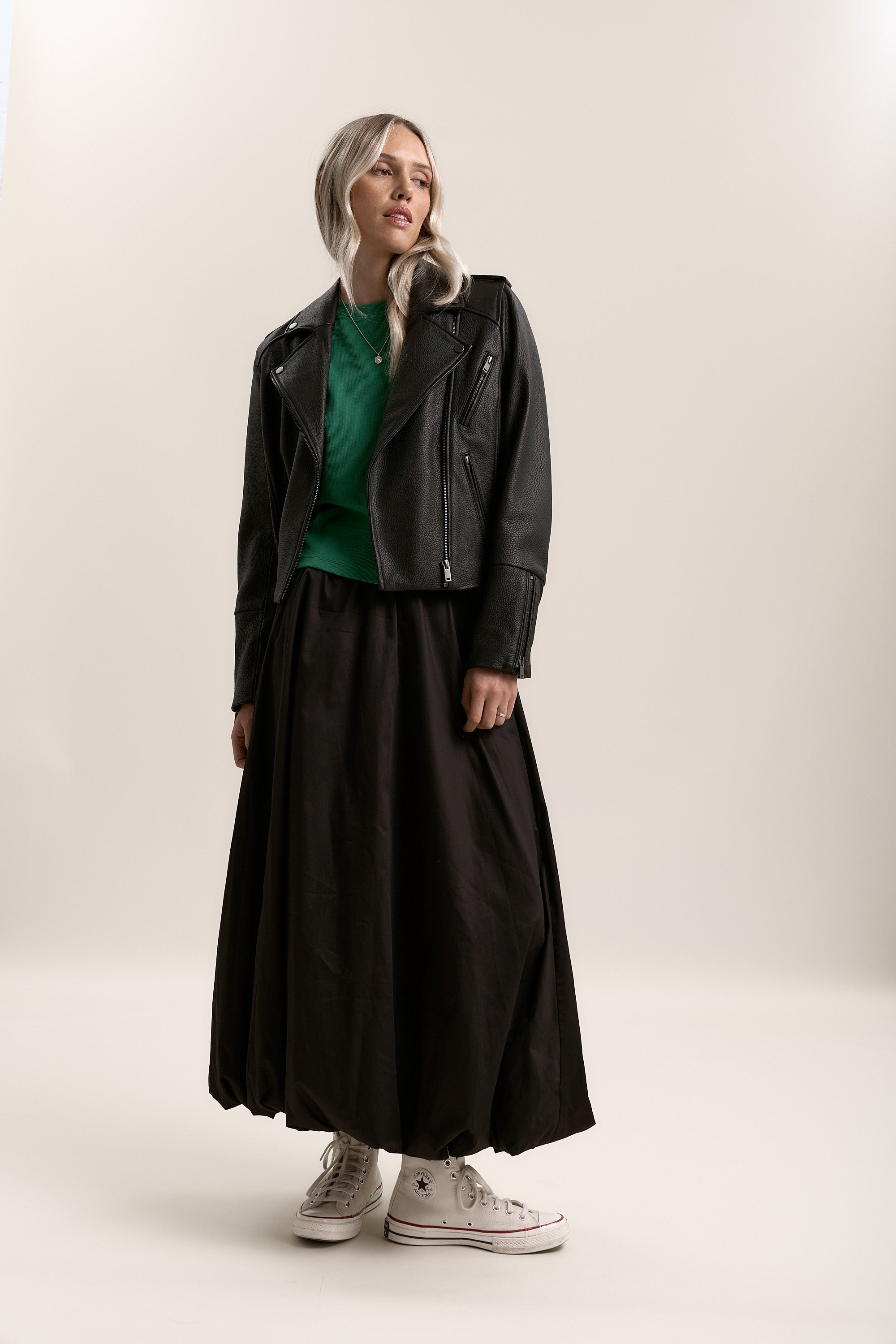 Woman in a green top, black jacket, Max Juniper Bubble Hem Skirt, and white sneakers.
