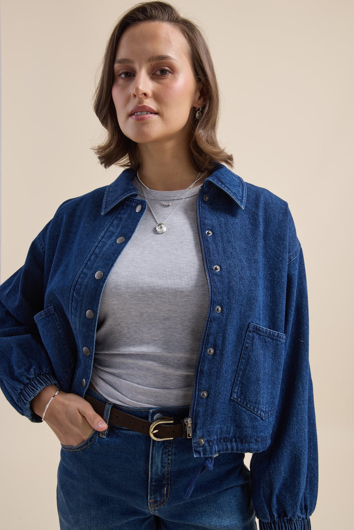 Woman in Elementary Relaxed Jacket stands against beige background, looking at camera.