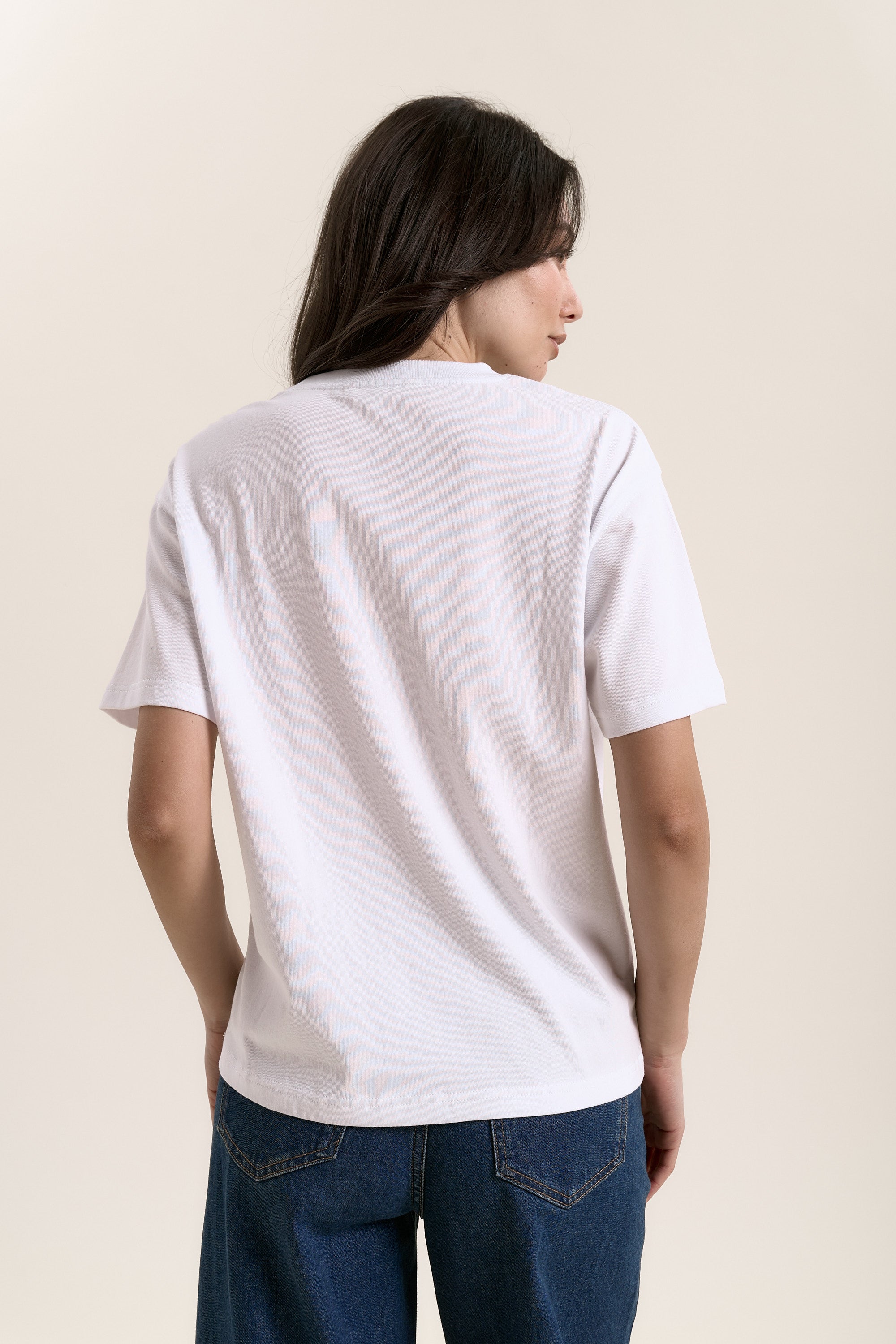 A woman in a Max Hold'em Tee and jeans, seen from the back.