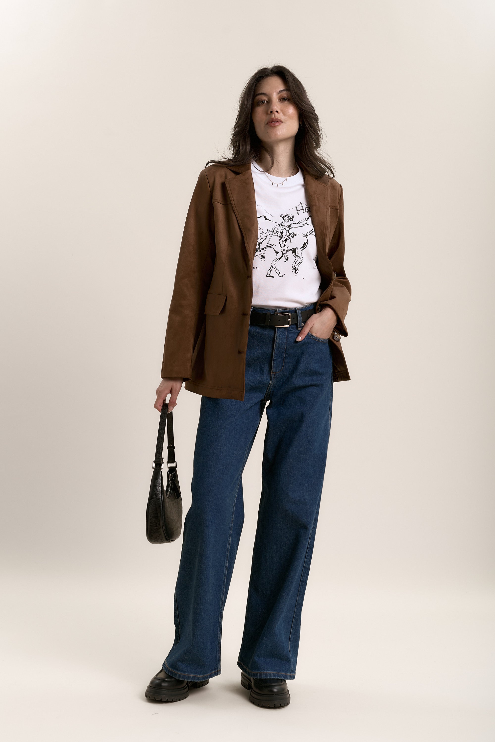 Woman in a brown blazer, Max Hold'em Tee, wide-leg jeans, and carrying a black handbag.