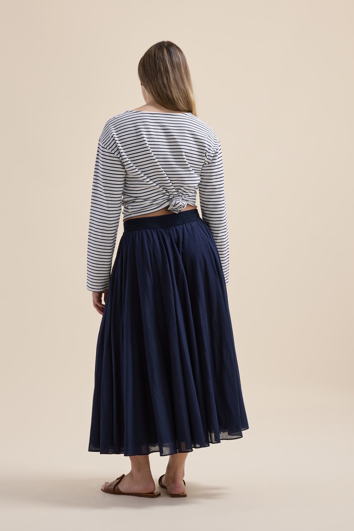 Woman in Elementary Gathered Skirt, striped top, and sandals stands against a beige background.