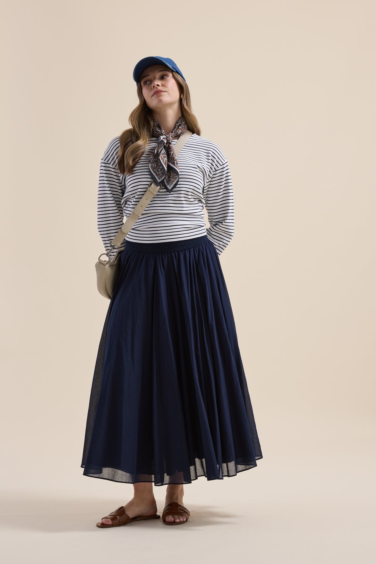 Woman in striped top, Elementary Gathered Skirt by Elementary, blue cap, scarf, bag & sandals poses.