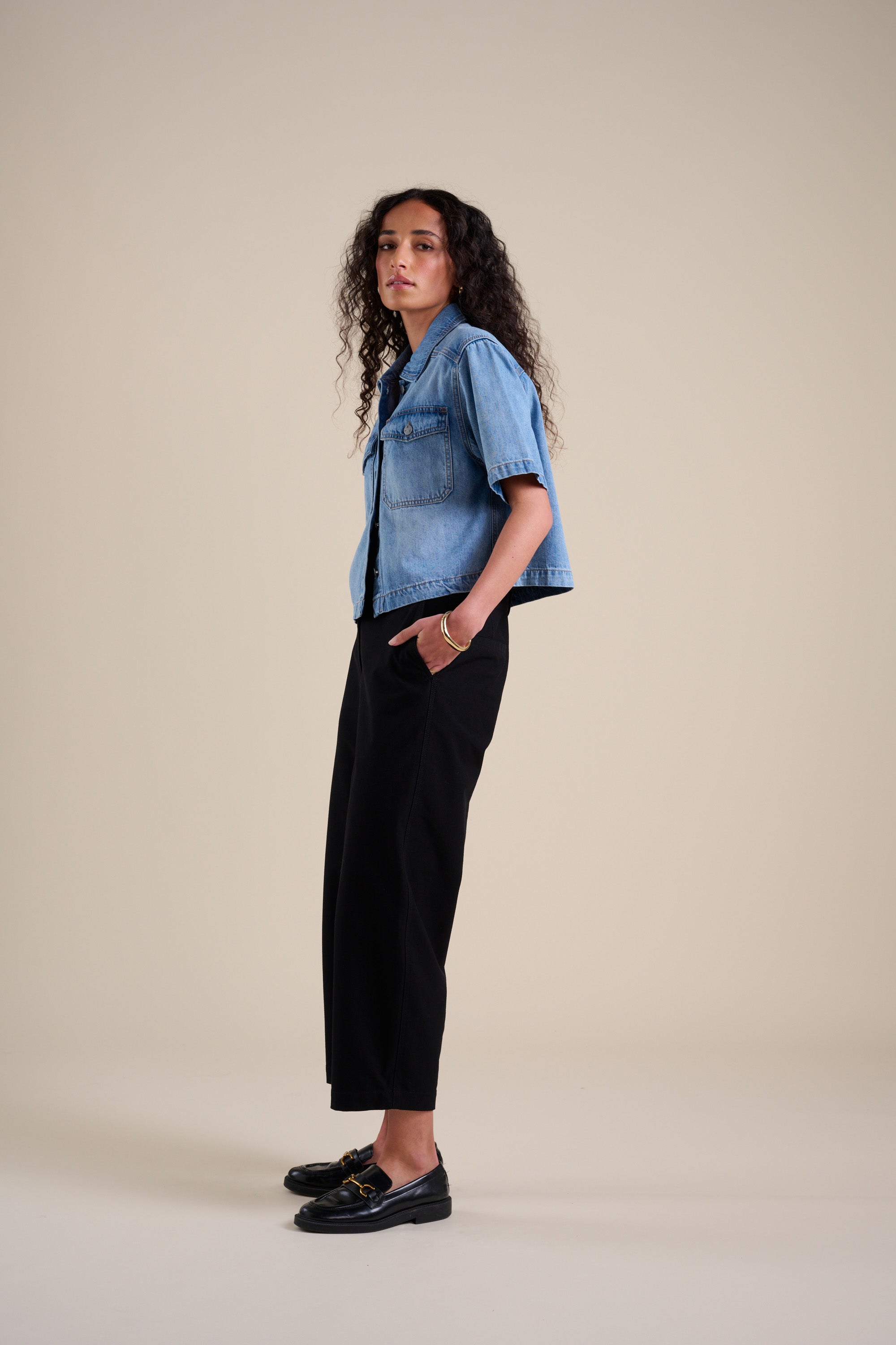 Woman in a denim shirt and Max Eden Barrel Leg Pants stands sideways against a beige background.