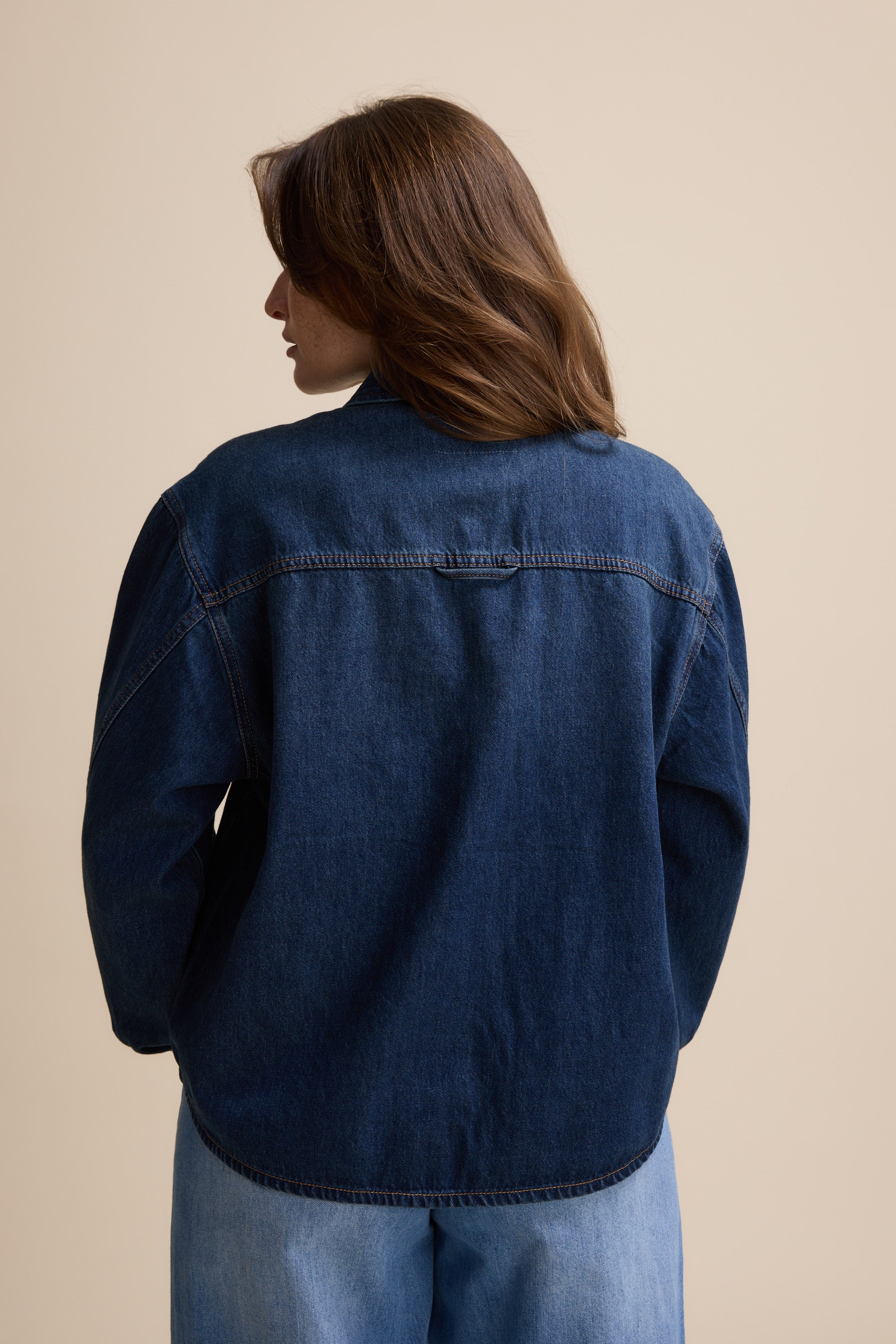 Person with brown hair in the Max Sabrina Cropped Denim Jacket, shown from the back on beige.