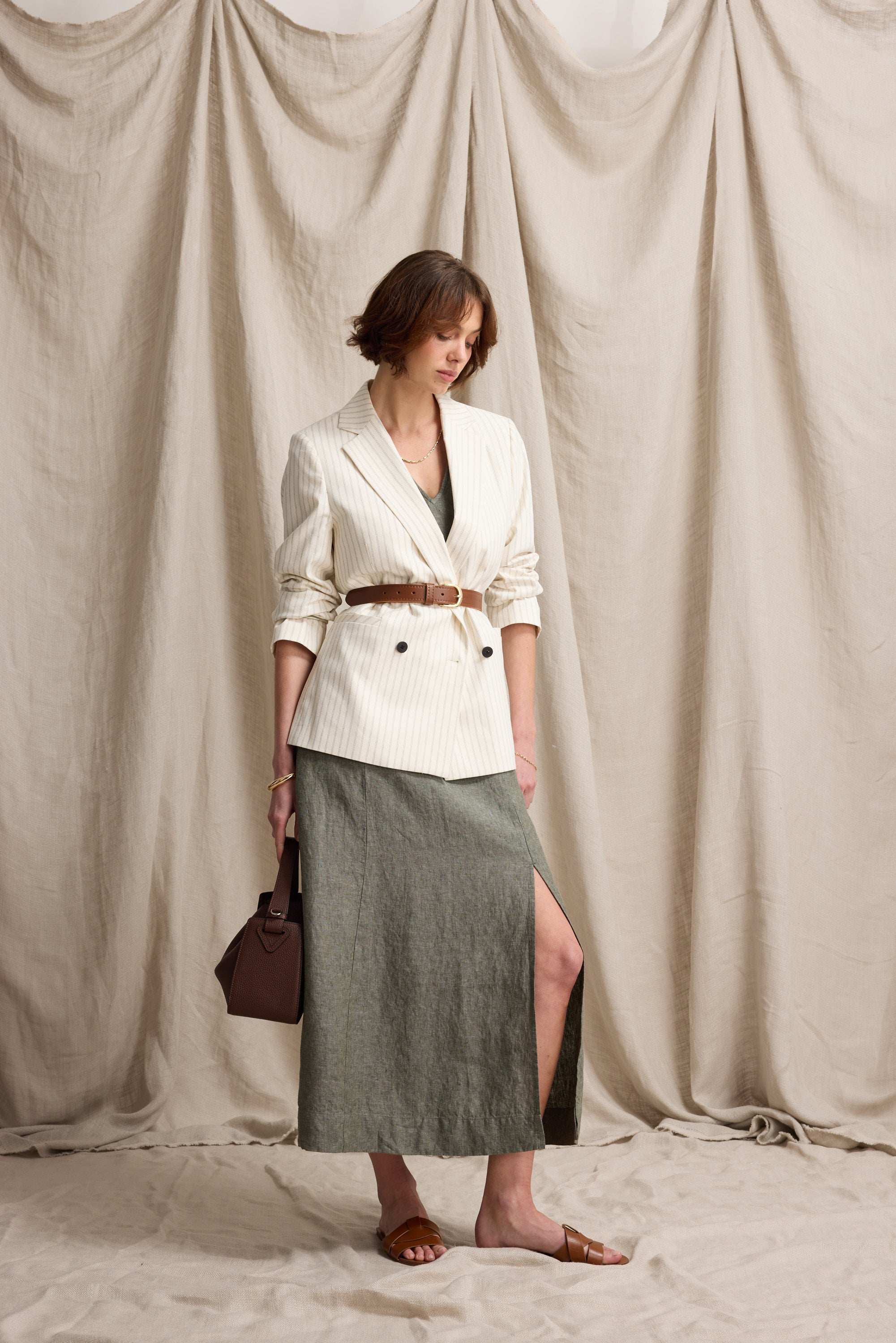 Woman wears Max's Alice V Neck Linen Dress before a beige draped fabric background.