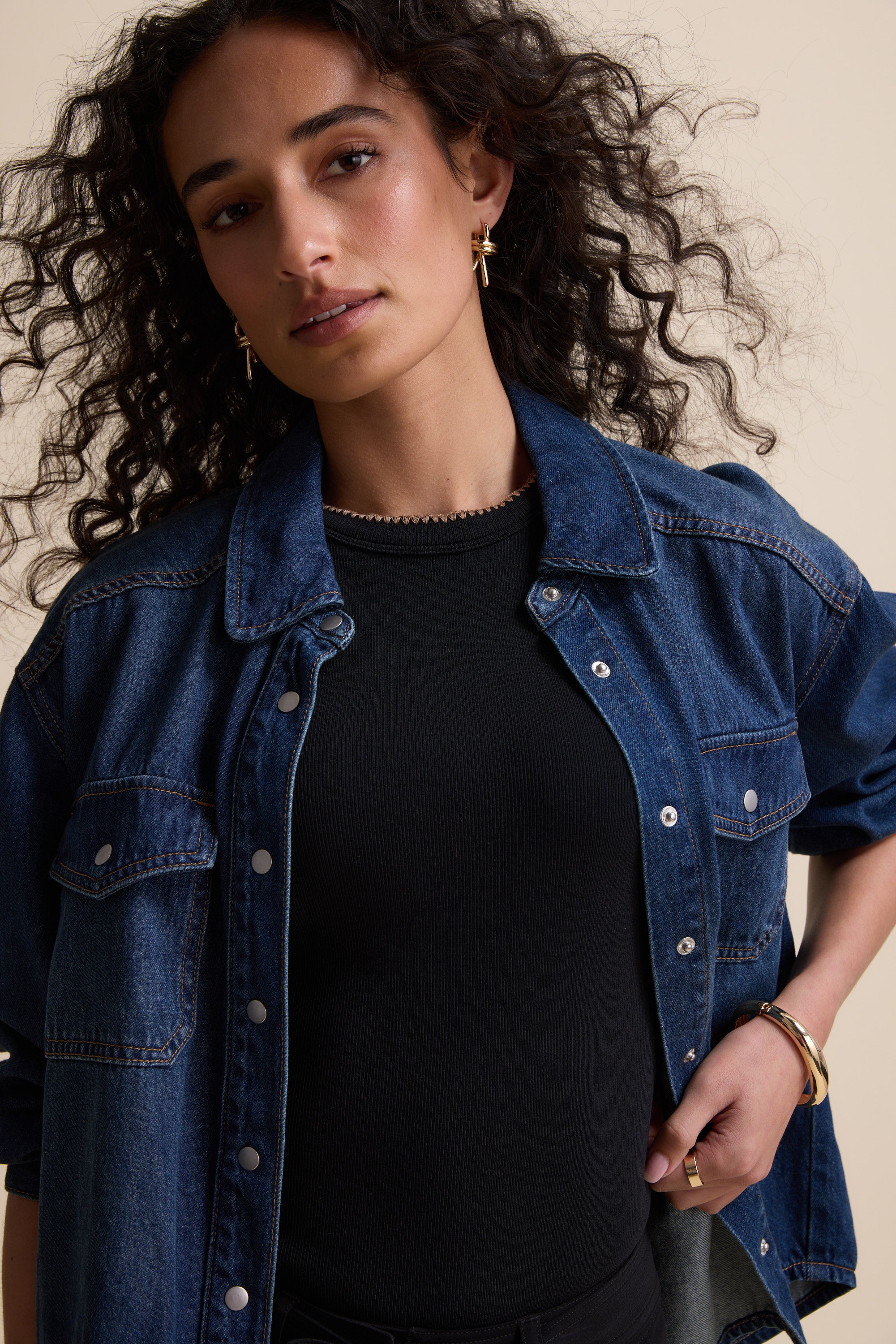 Woman with curly hair in a denim jacket wears Max's The Stitch Detail Tank, looking at camera.