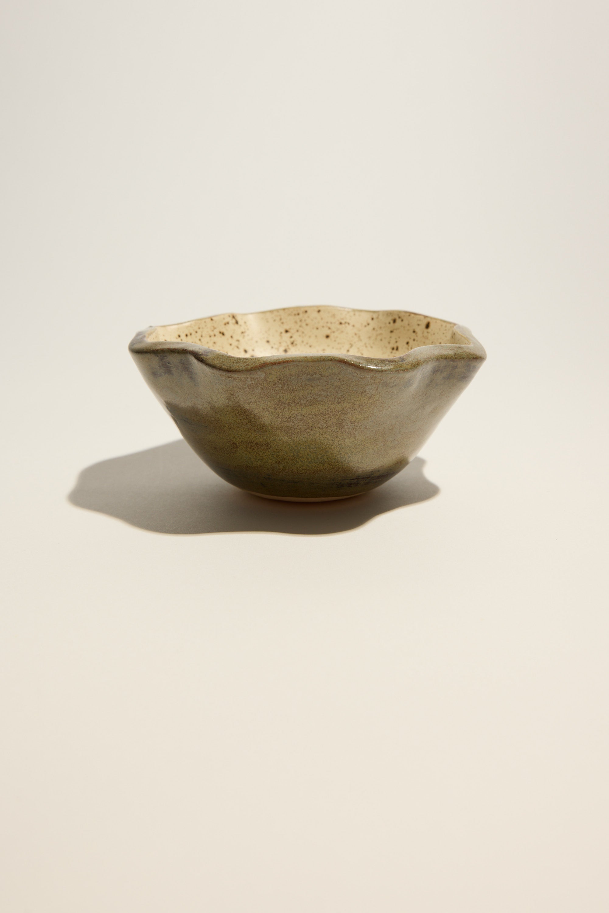 The Magnolia Lane Ruffled Condiment Bowl by Magnolia Lane features an irregular rim, speckled beige interior, and mottled green-brown exterior, showcasing artisanal style on a light surface with a soft shadow. Handmade in New Zealand.