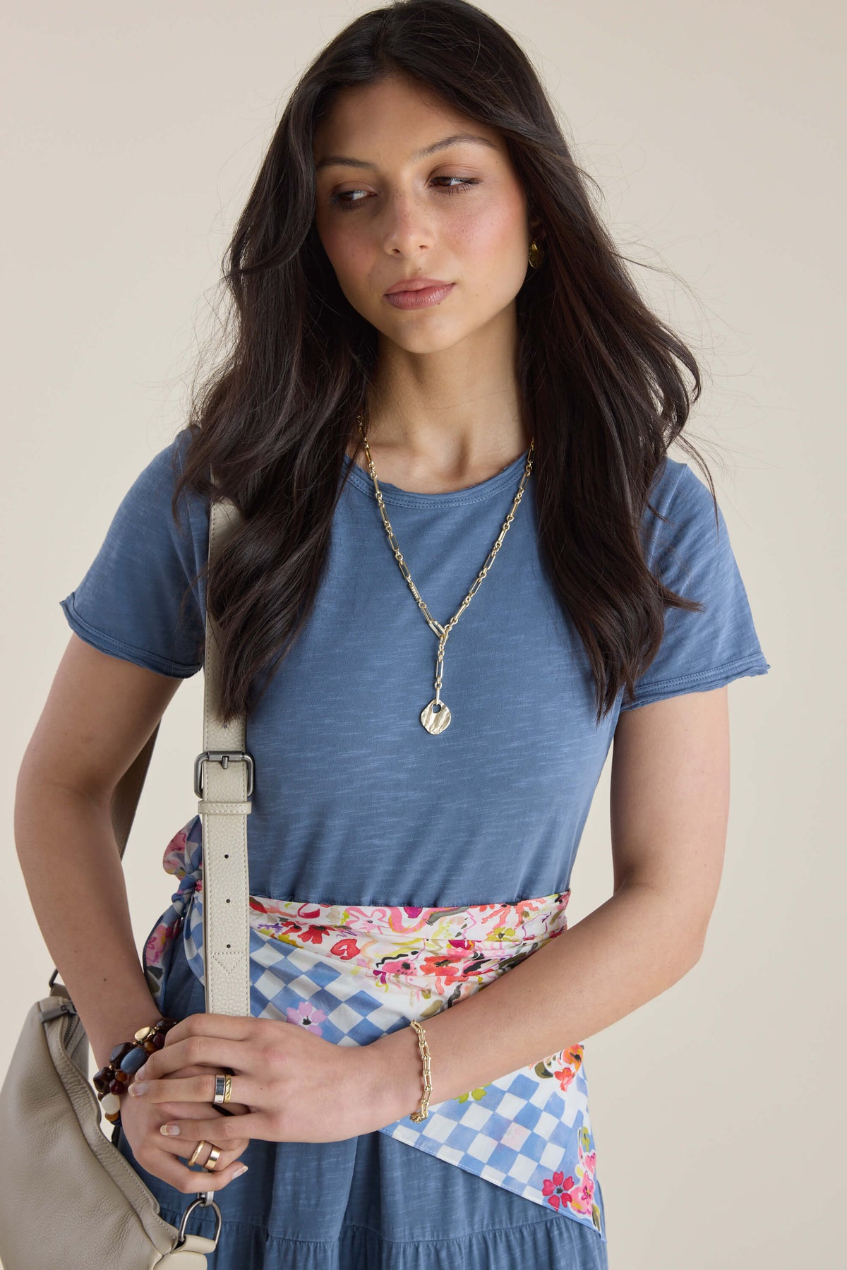 Woman in Elementary Jersey Tiered Dress, blue shirt, floral skirt, gold jewelry, and bag.