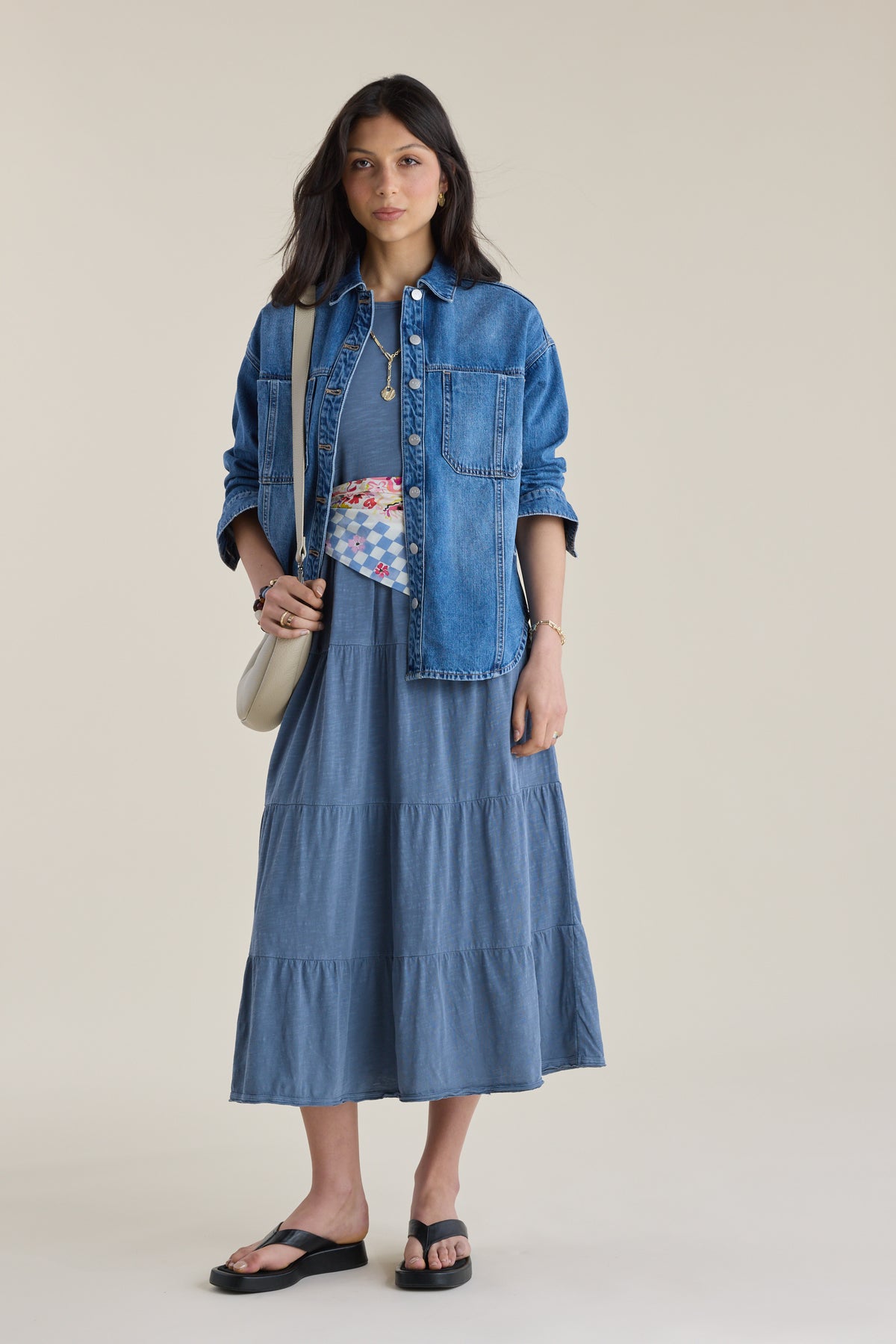 Woman in the Elementary Jersey Tiered Dress, denim jacket, sandals, belt, and crossbody bag.