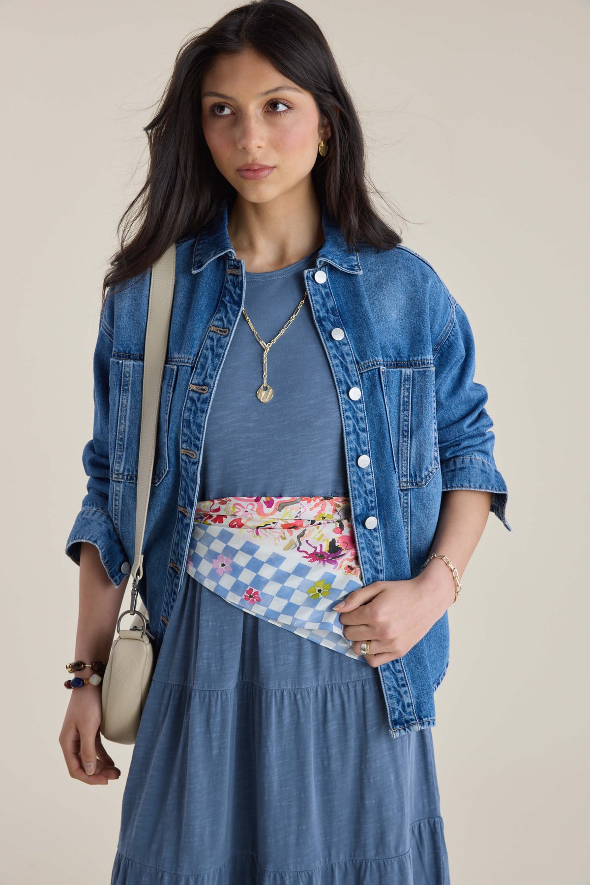 Woman in Elementary Jersey Tiered Dress, denim jacket, crossbody bag, and patterned waist scarf.