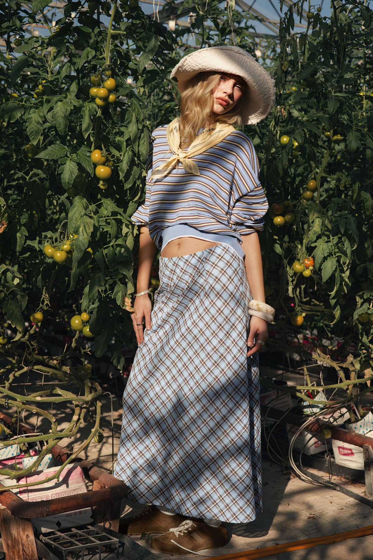 Woman in striped top, Max The Perfect Slip Skirt, and hat among tomato plants in a greenhouse.