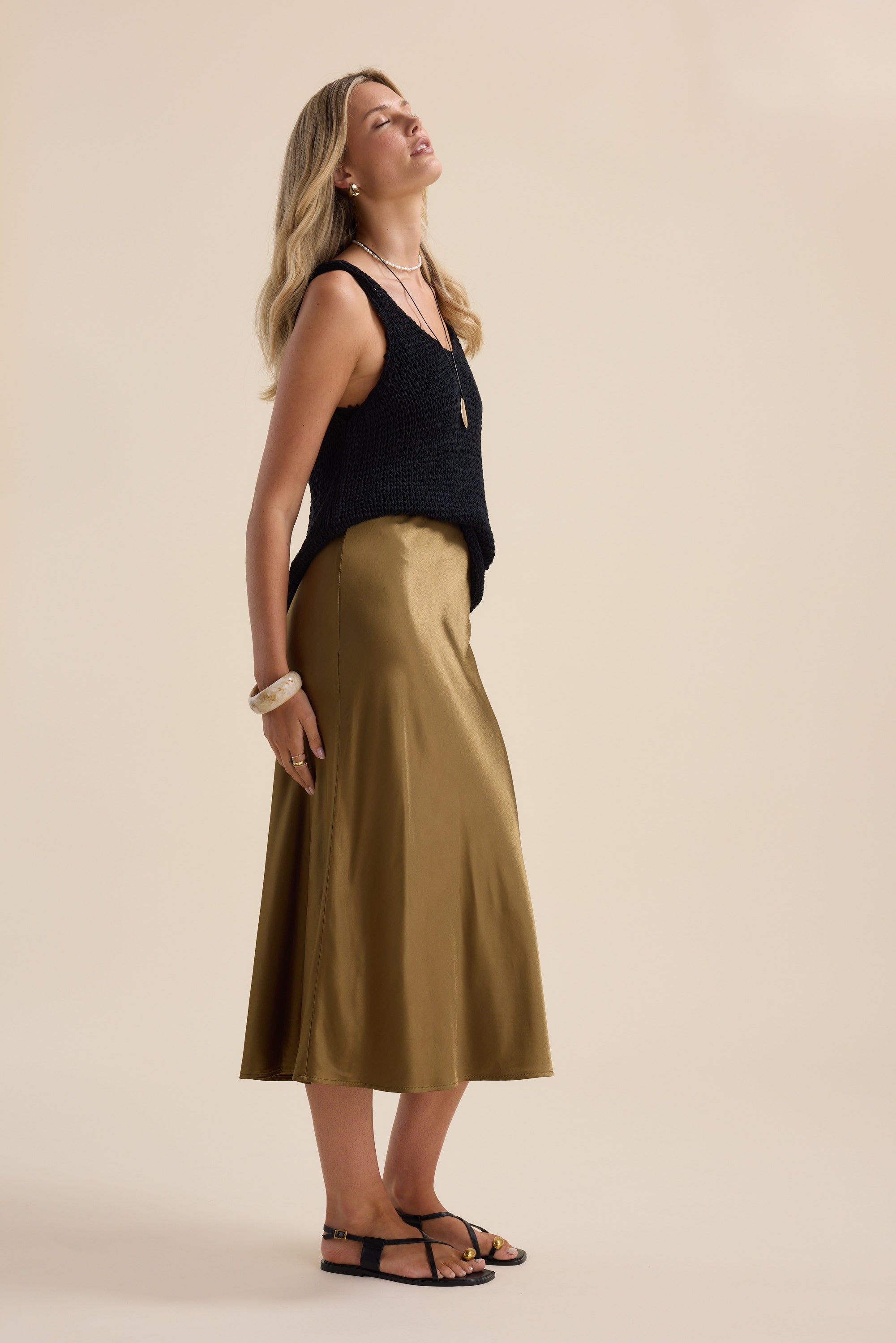 Woman in Max Lana Chunky Knit Tank stands sideways on beige background.