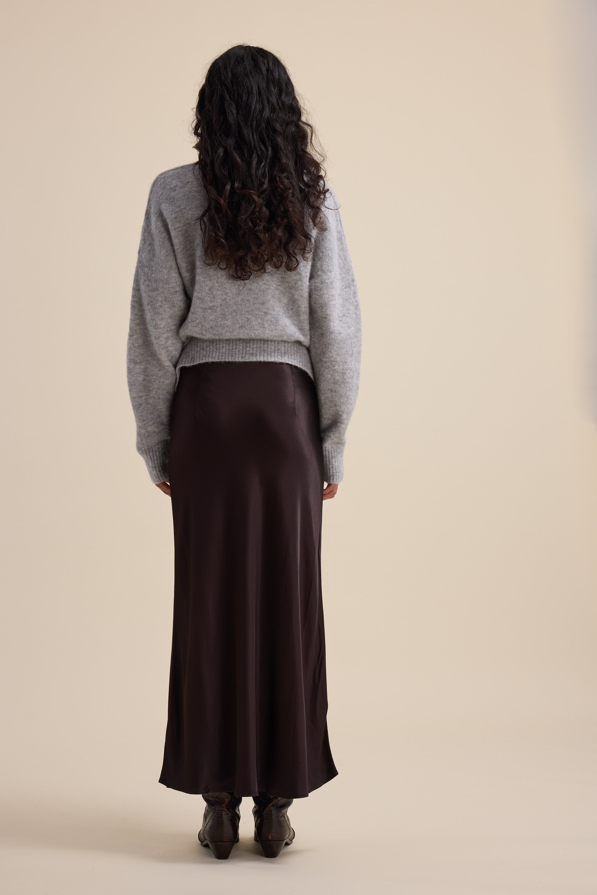 Person with long curly hair wears Max's The Perfect Slip Skirt and a gray sweater, facing away.