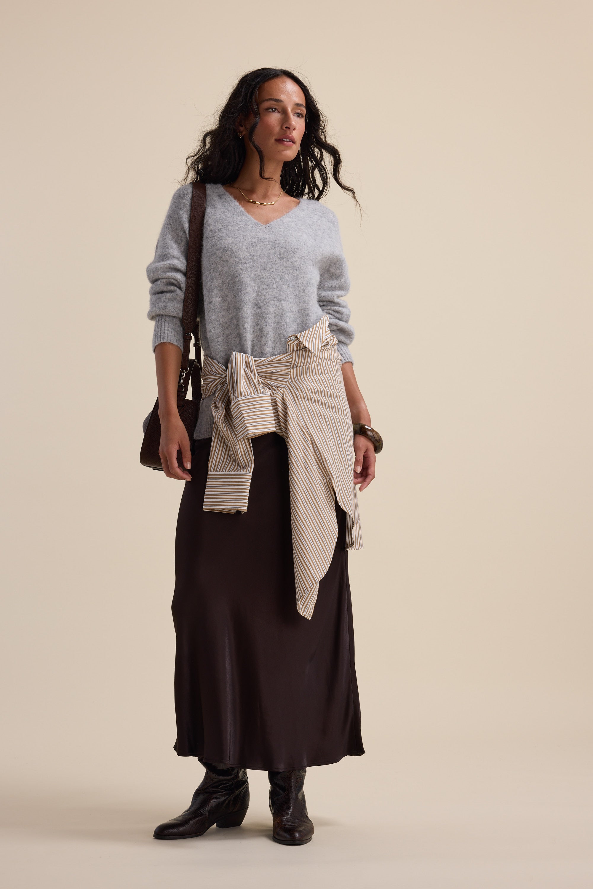 Woman in a grey sweater, Max The Perfect Slip Skirt, boots, with a striped shirt at her waist.