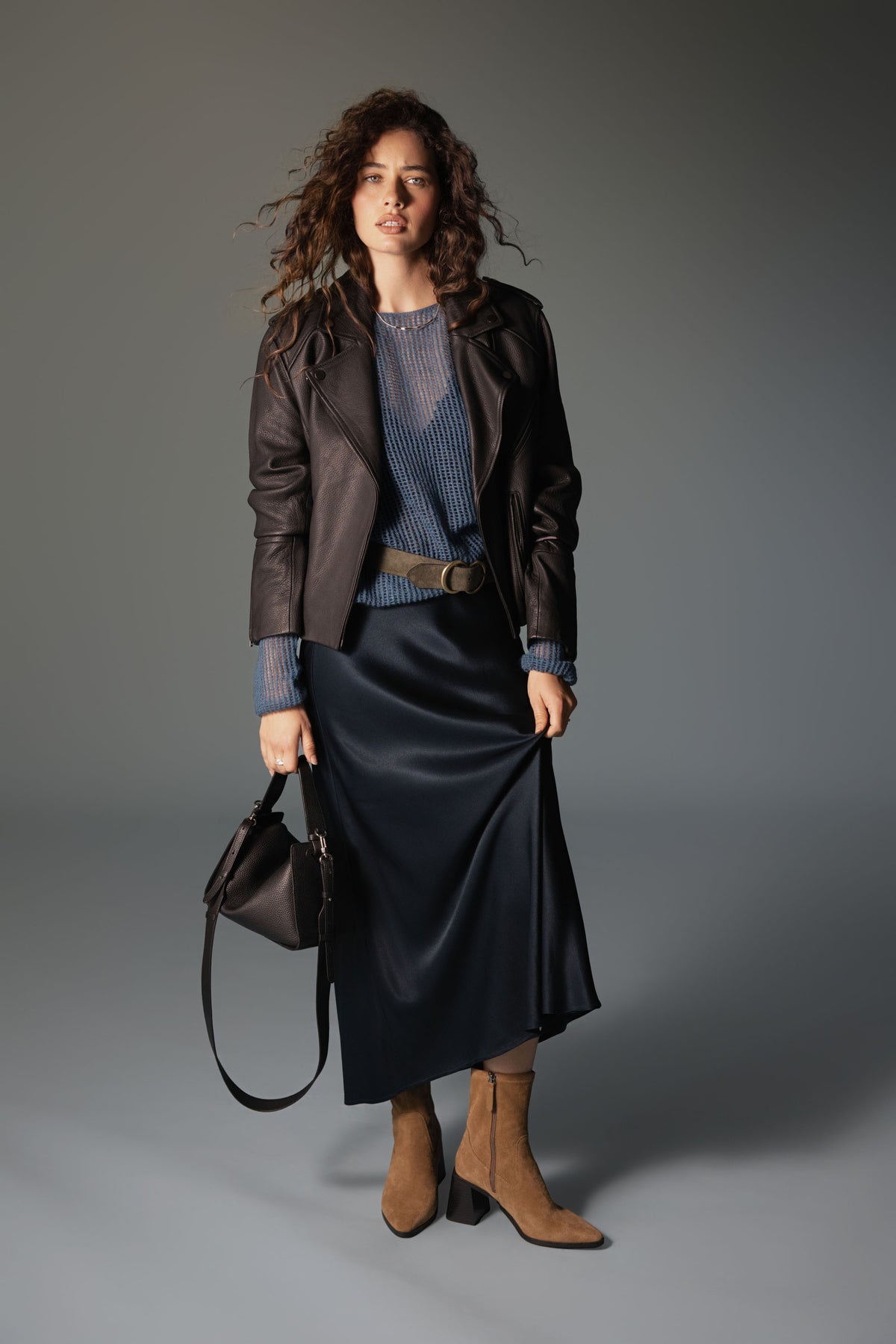 Woman in leather jacket, blue top, Max The Perfect Slip Skirt, brown boots, black handbag.