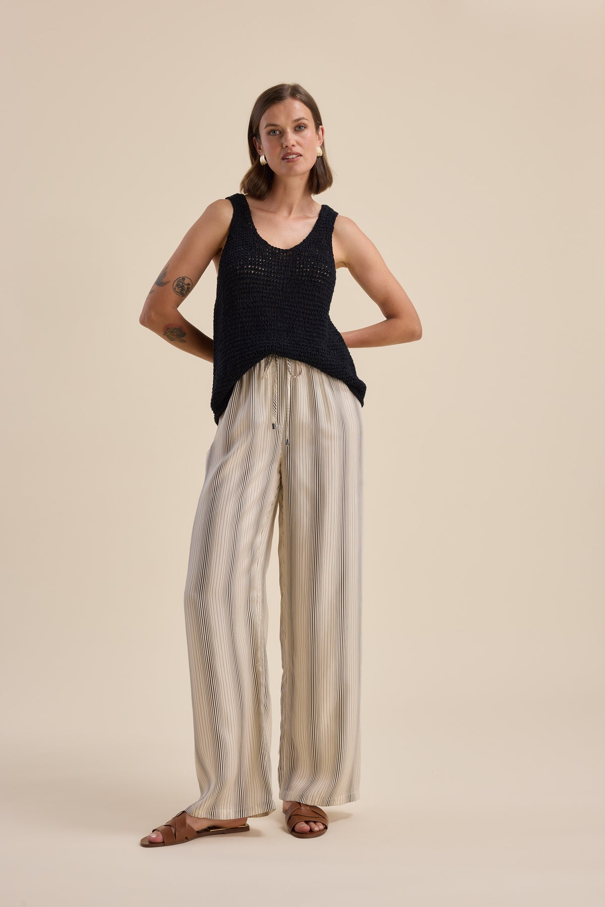 Woman wears Max Sera Drawstring Pants with a black sleeveless top on beige background.