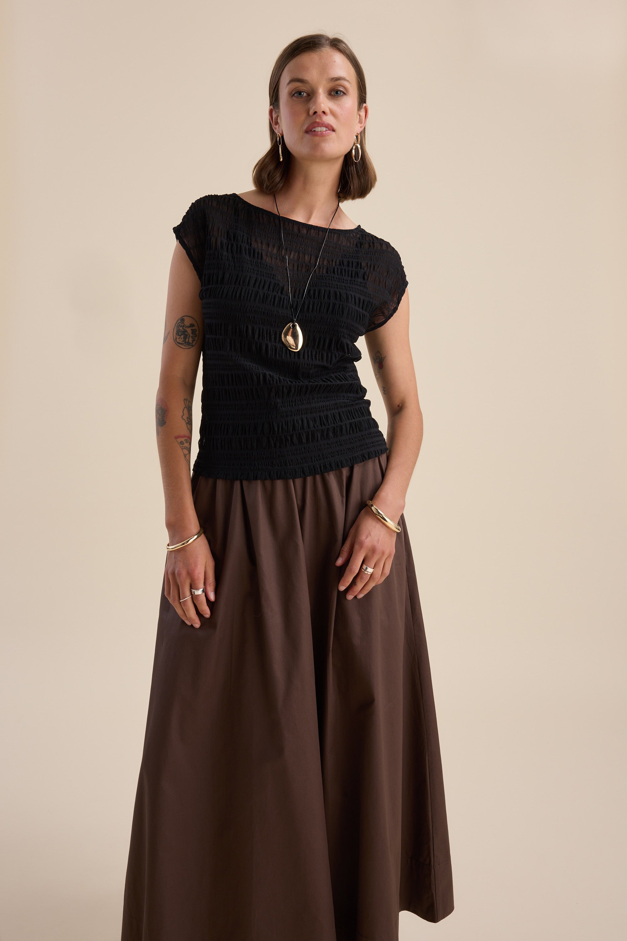 Woman wears Max Willow Textured Mesh Tee and brown skirt against a beige background.