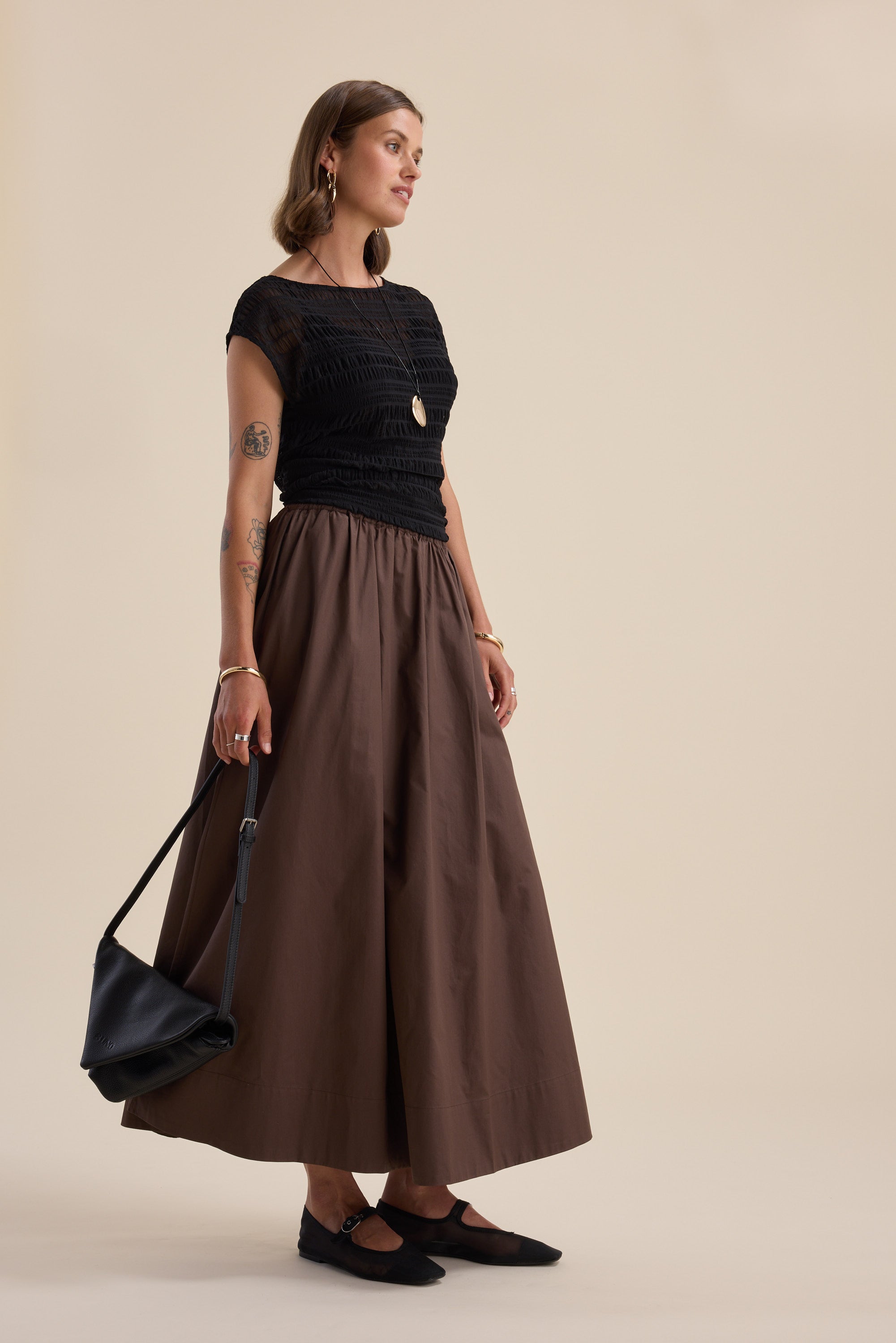 Woman in a Max Willow Textured Mesh Tee and brown skirt with a black bag, beige background.