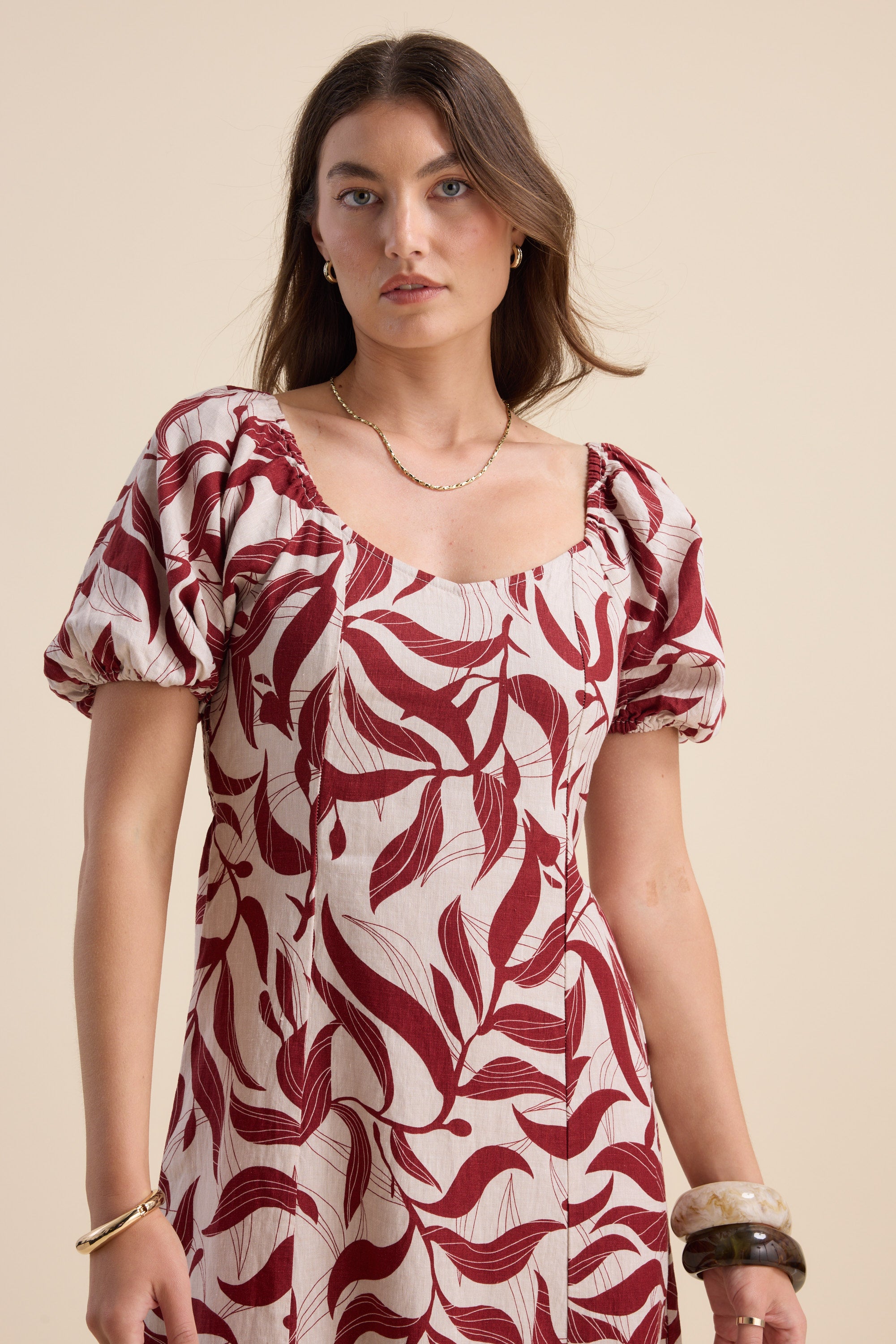 Woman wears the Max Camille Puff Sleeve Dress with a botanical print against a beige background.