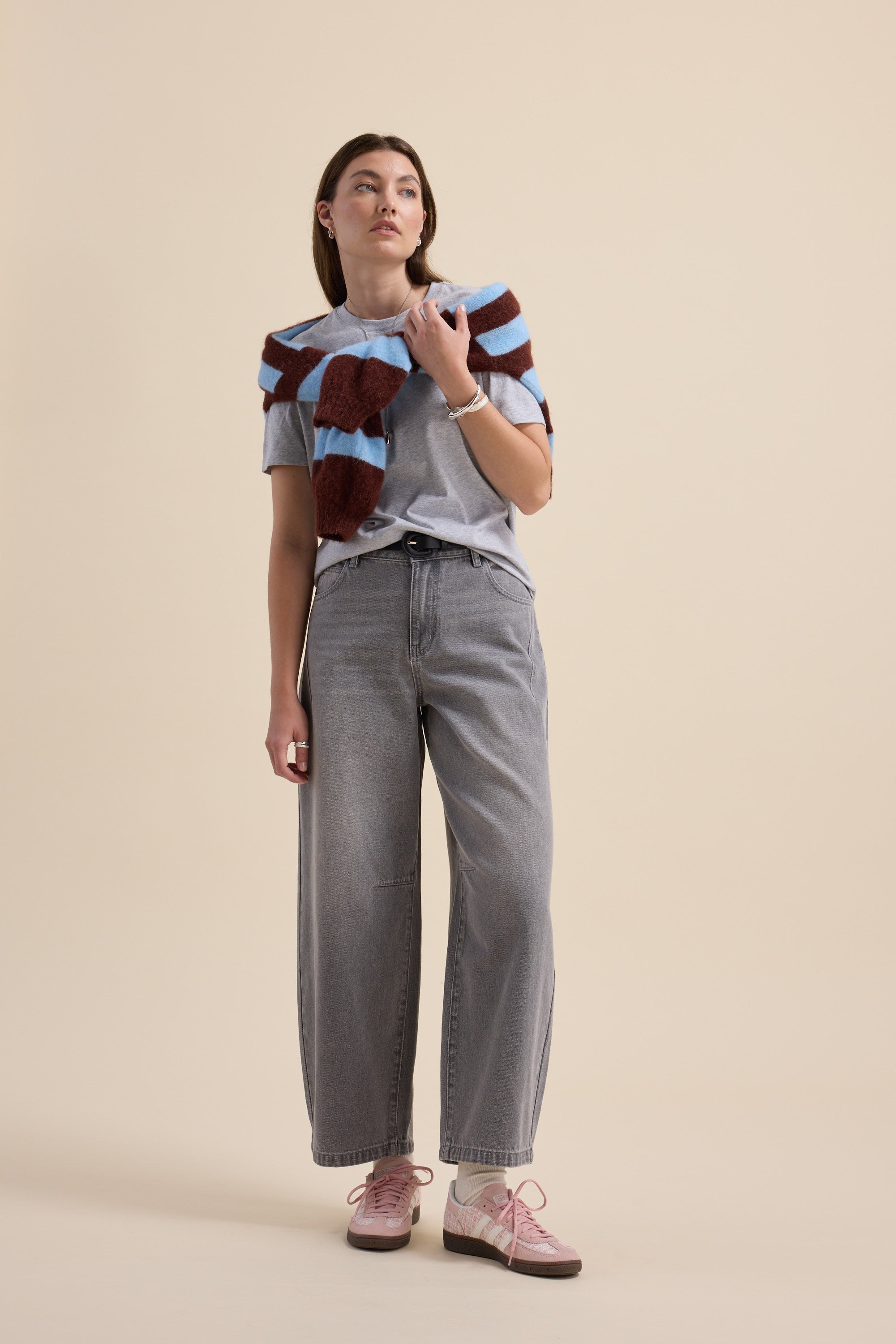 Woman in gray tee, Max The Barrel Leg Jeans, striped sweater, and pink sneakers poses.