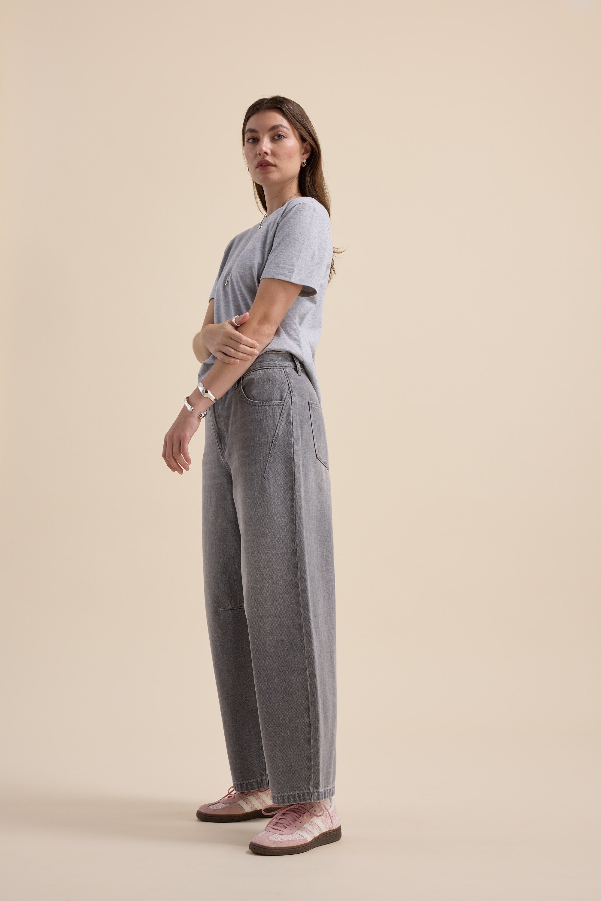 Woman in Max’s The Barrel Leg Jeans and grey t-shirt, standing sideways against beige background.