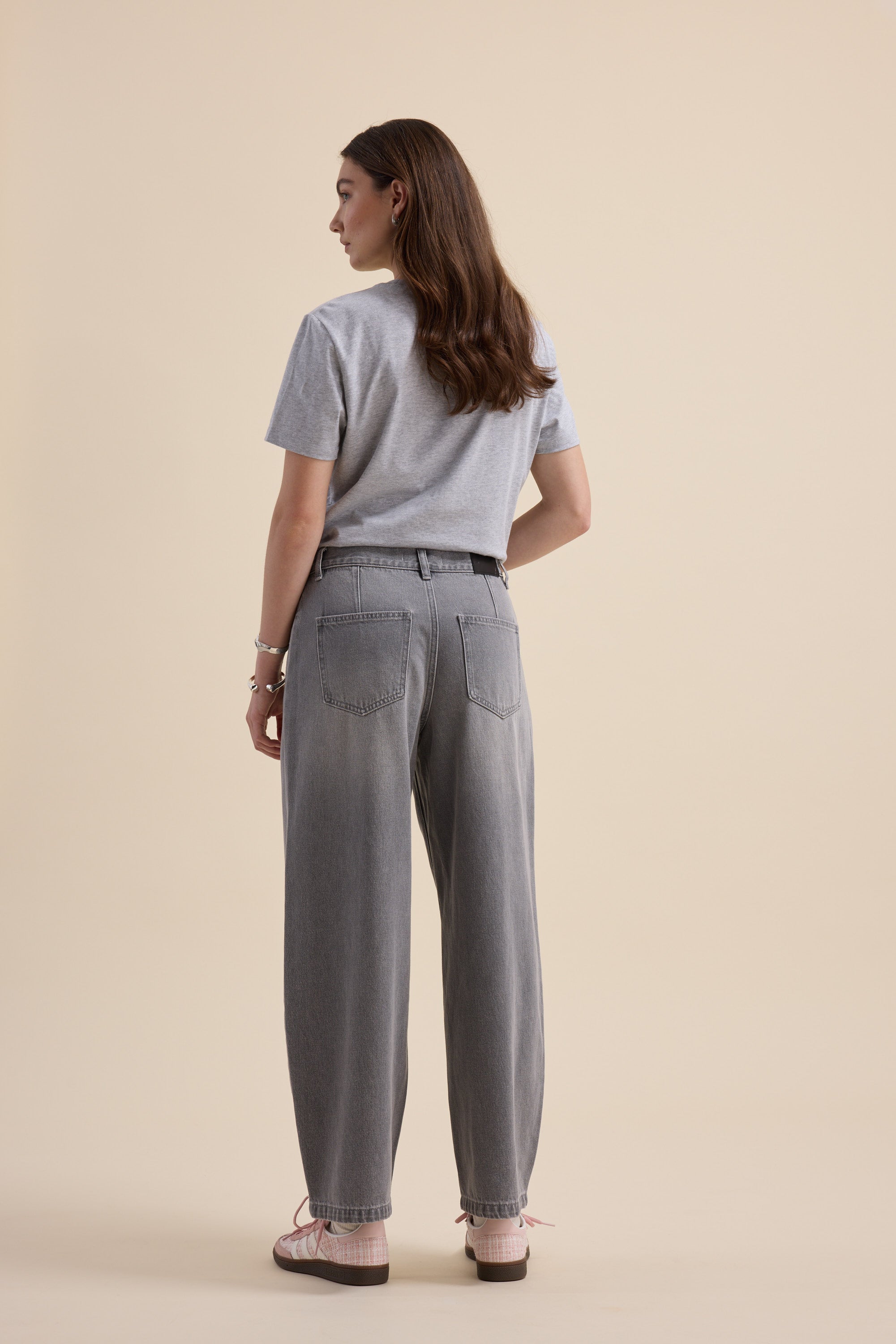 Woman wears Max The Barrel Leg Jeans and gray t-shirt, facing away from the camera.