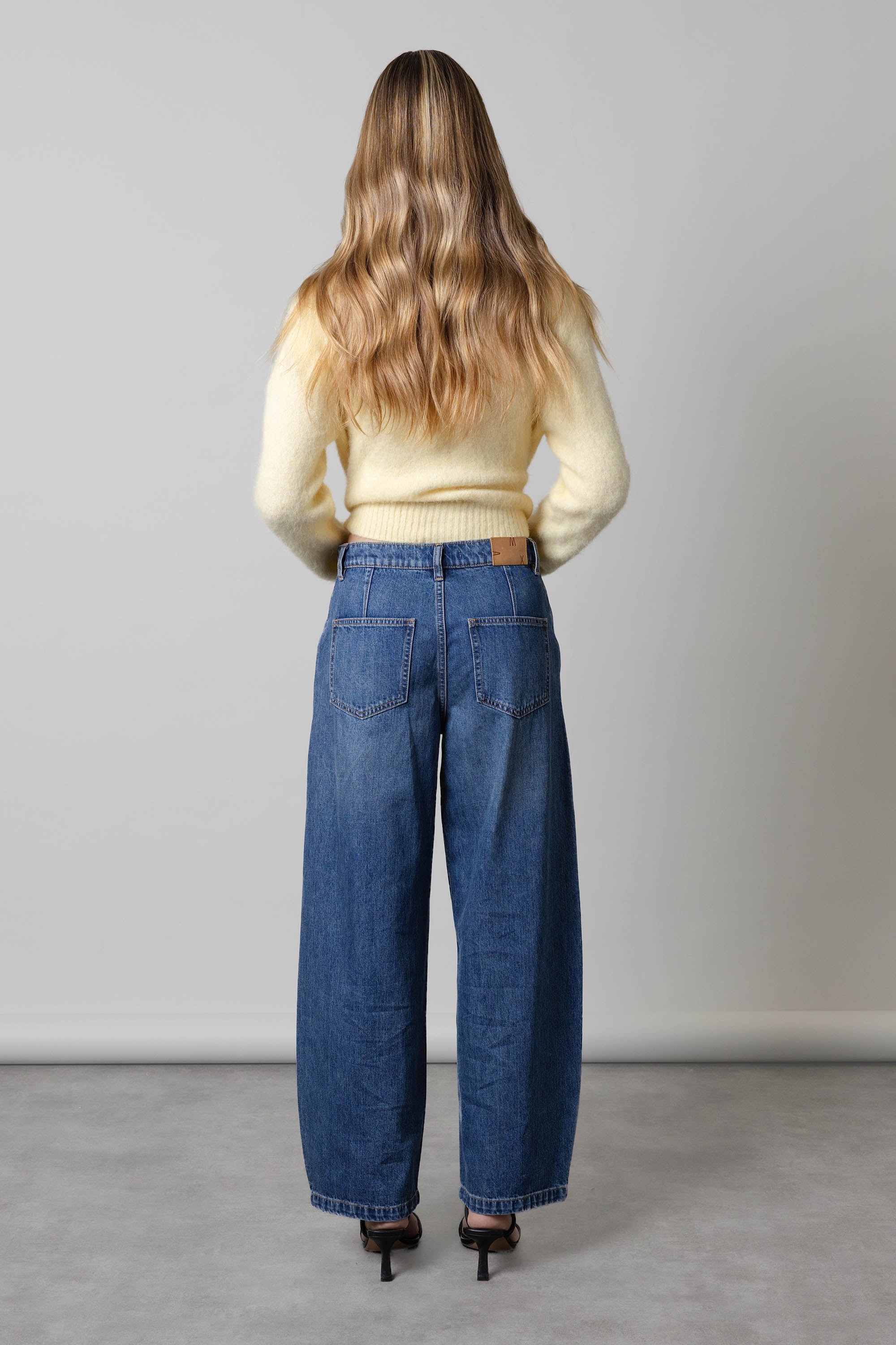 Woman in yellow sweater and Max The Barrel Leg Jeans, long wavy hair, facing backward.