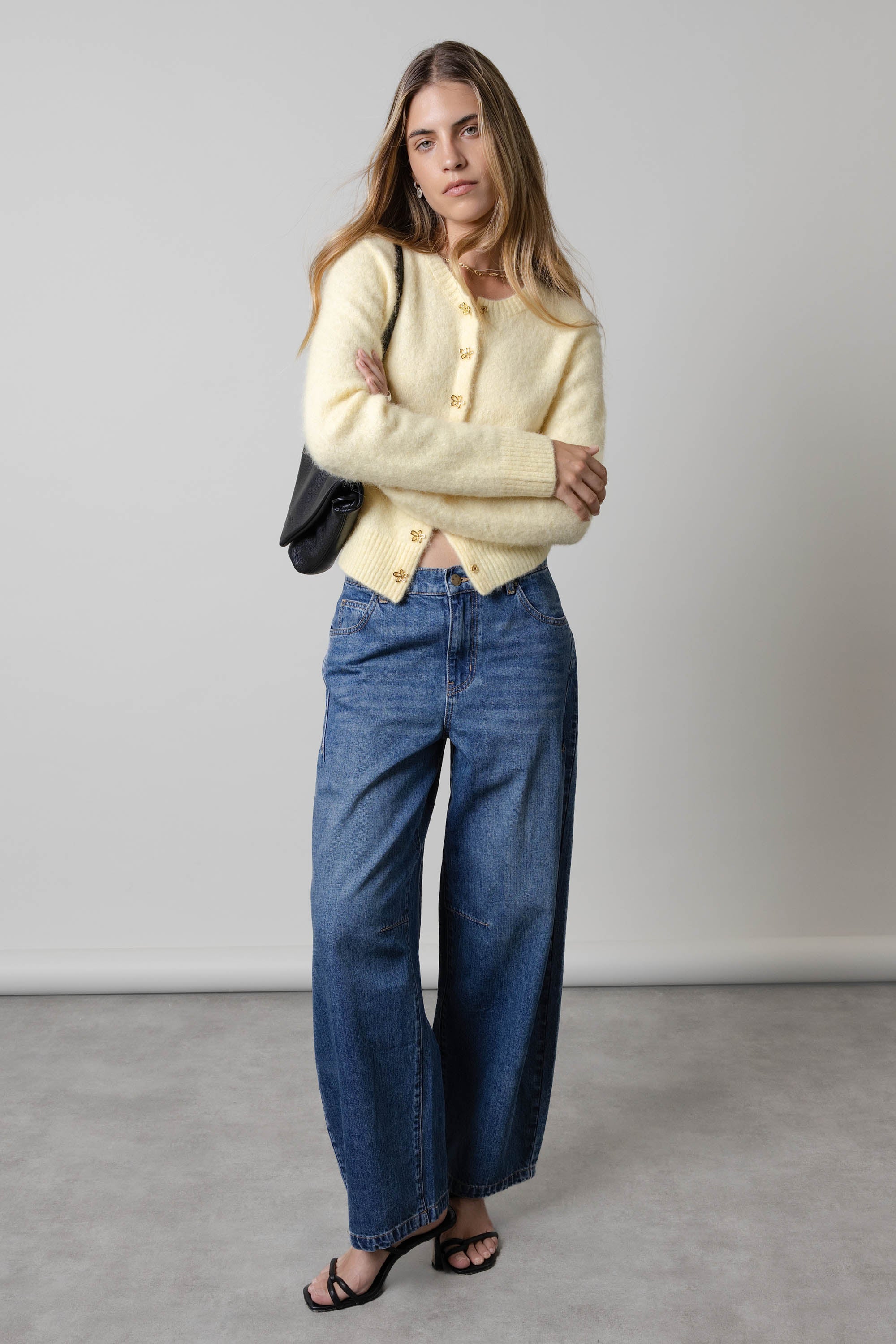 Woman in Max The Barrel Leg Jeans, yellow cardigan, black sandals, and shoulder bag indoors.