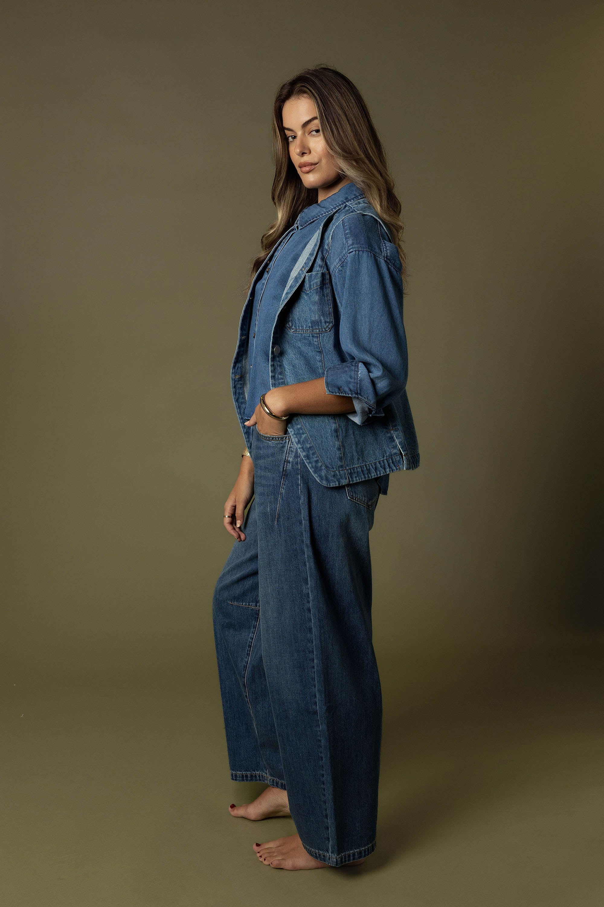 Barefoot woman wears Max's The Barrel Leg Jeans against a plain olive background.