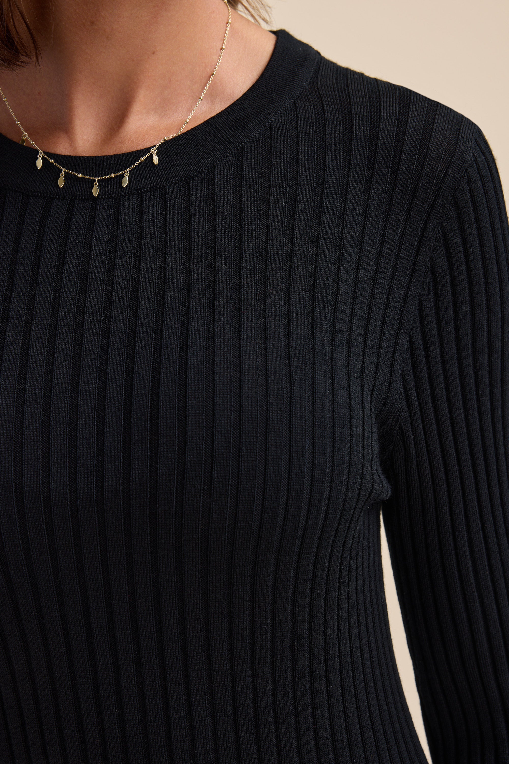 A person wearing the Elementary ZQ Merino Crew Neck Top and a delicate gold charm necklace.
