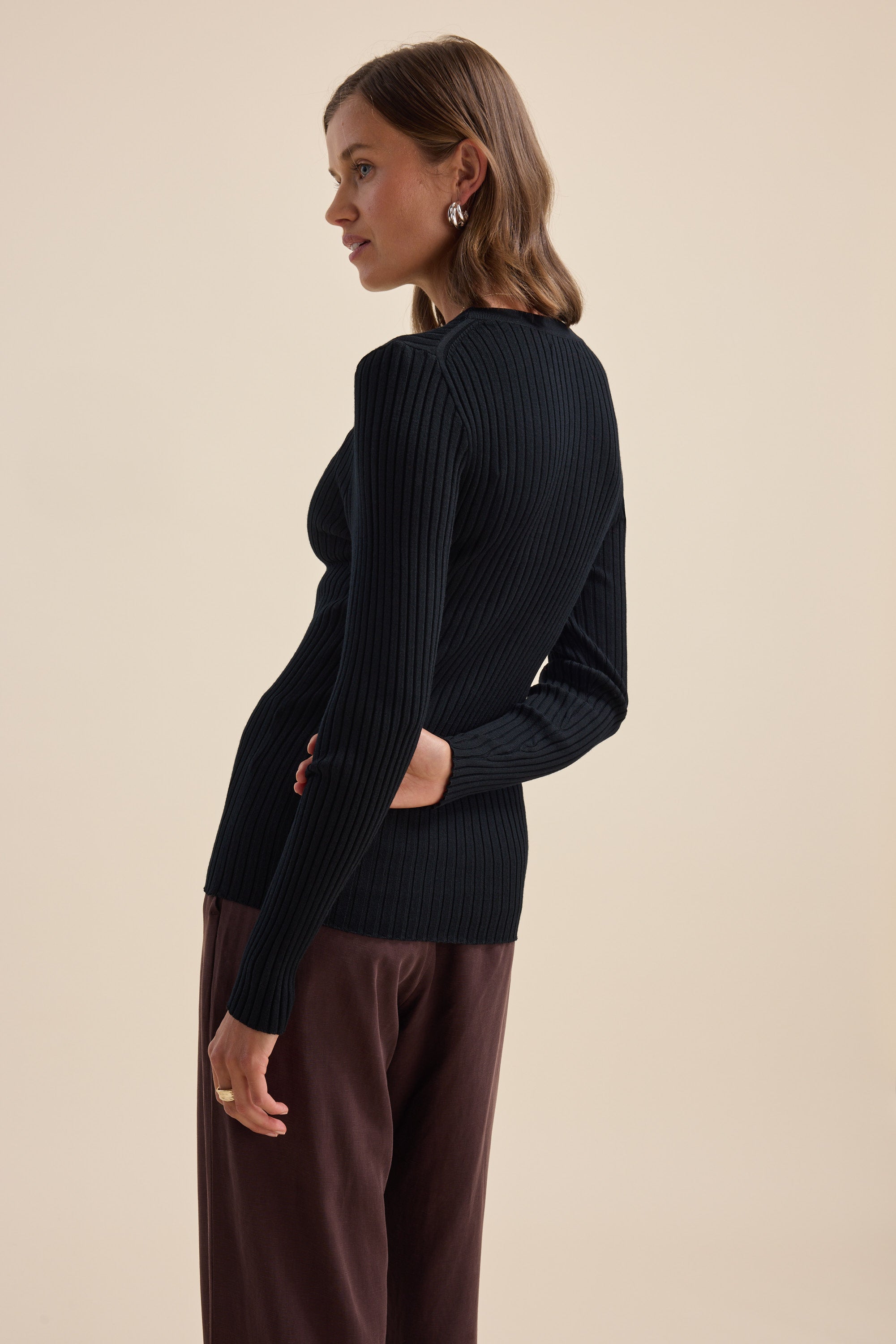 Woman in an Elementary ZQ Merino Crew Neck Top and brown pants against a beige background.