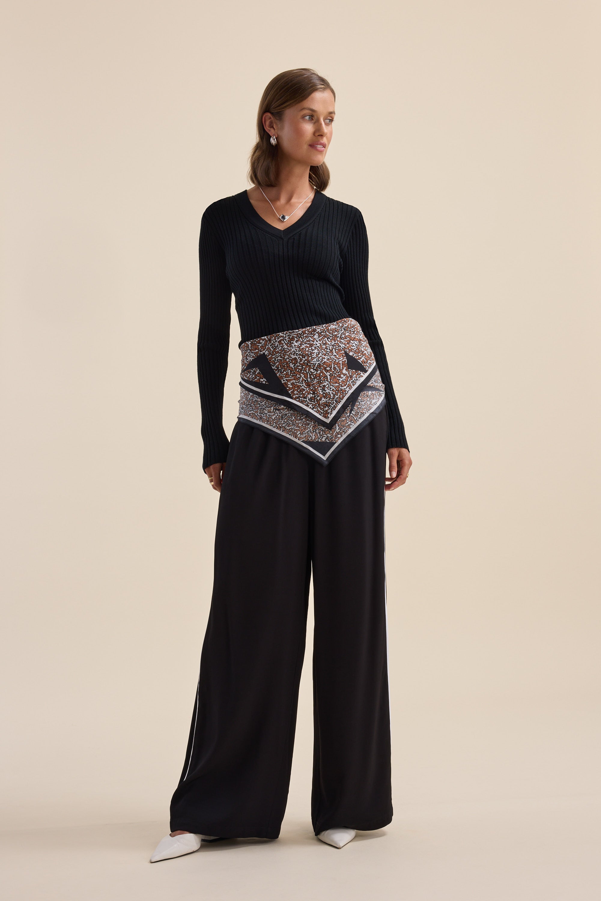 Woman in Elementary ZQ Merino V Neck Top, wide pants, patterned scarf, and white heels.