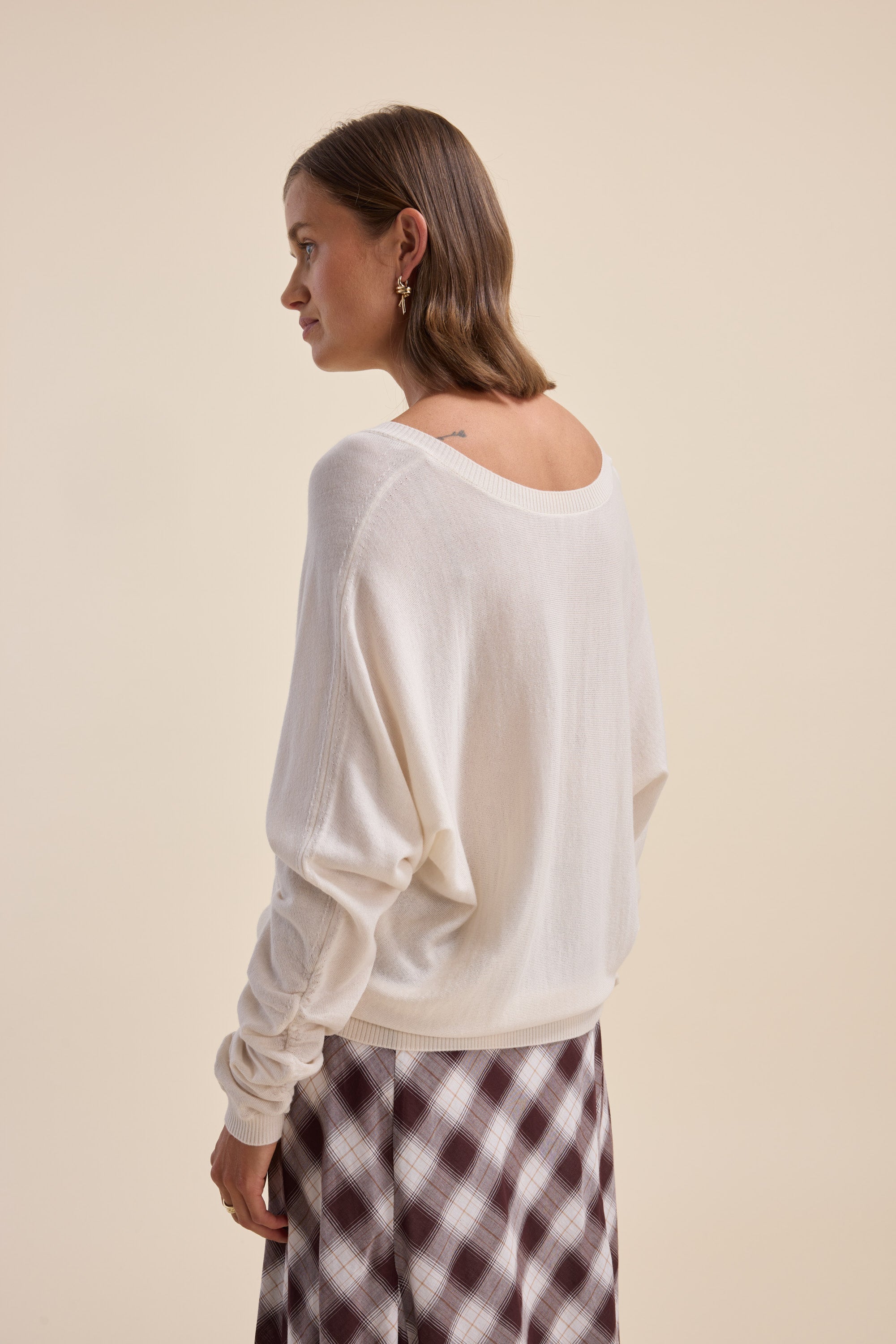 Woman in Elementary ZQ Merino Reversible Sweater facing sideways against a beige background.