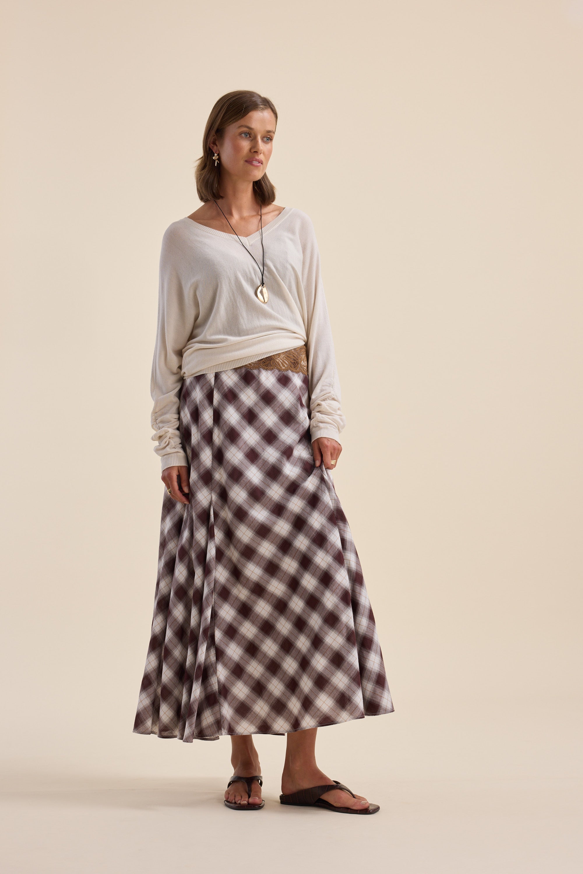 Woman in Elementary ZQ Merino Reversible Sweater, plaid maxi skirt, sandals, and jewelry.
