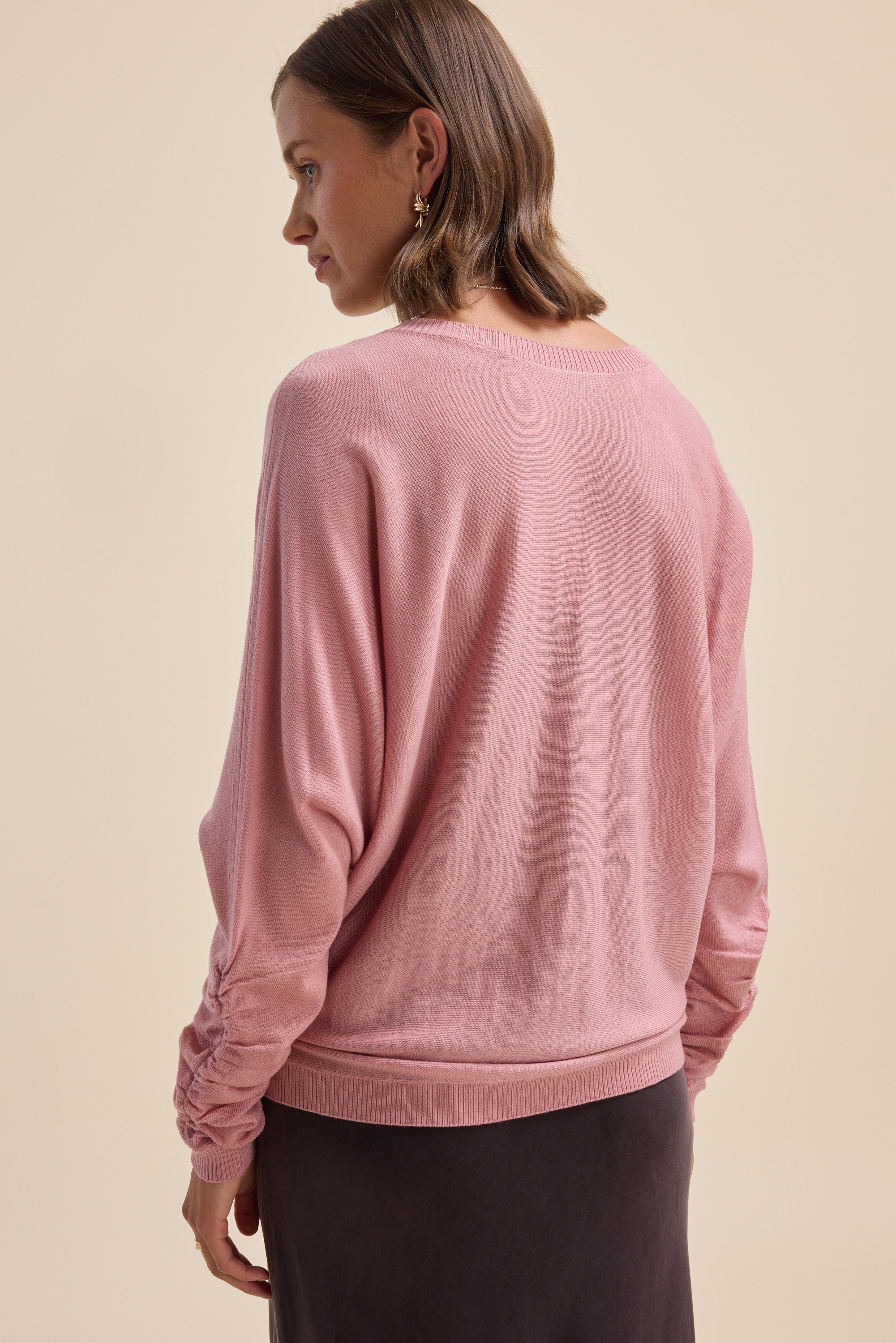 Woman wears Elementary ZQ Merino Reversible Sweater in pink with dark skirt, back view.