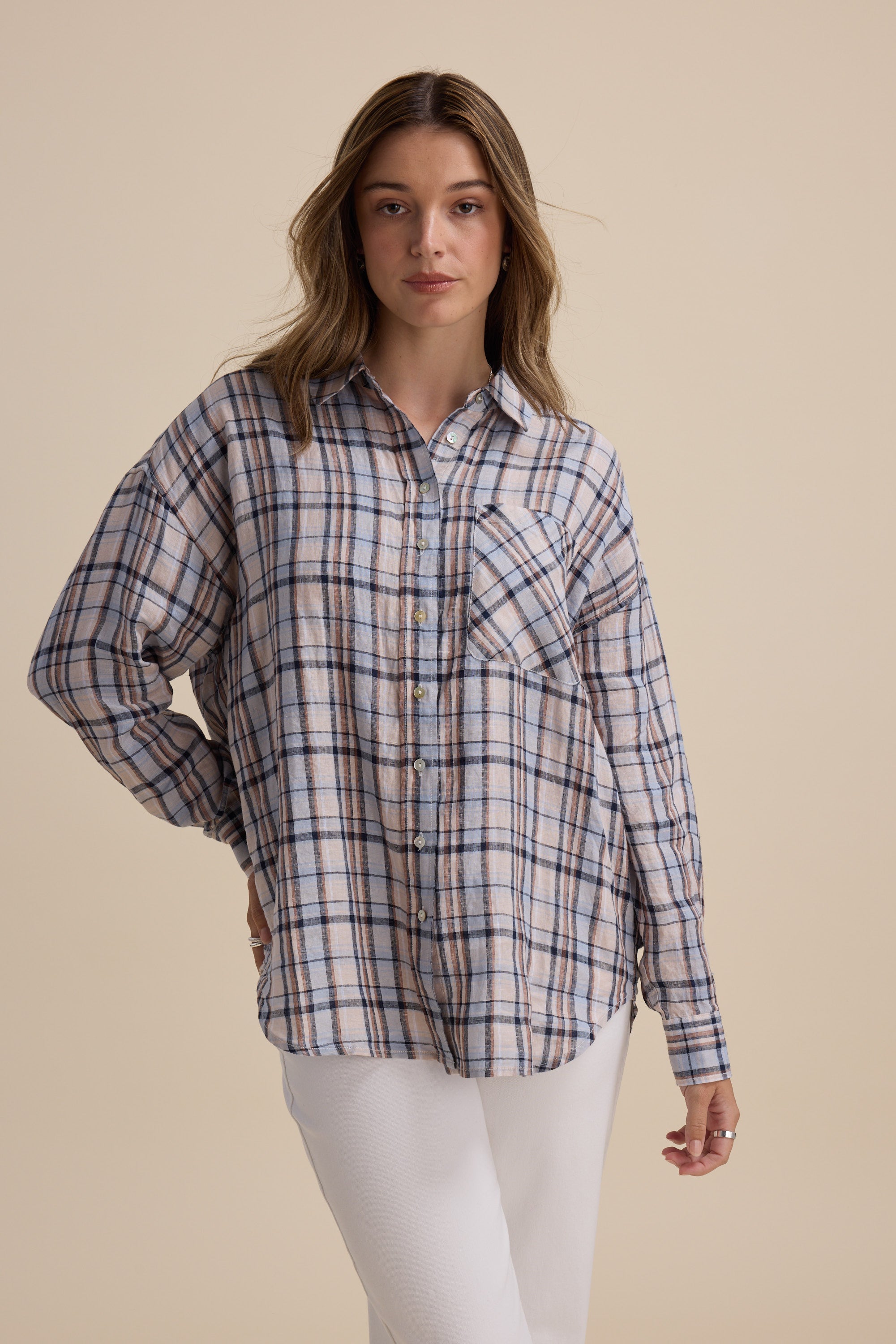 Woman in the Elementary Oversized Shirt stands against a plain beige background in white pants.