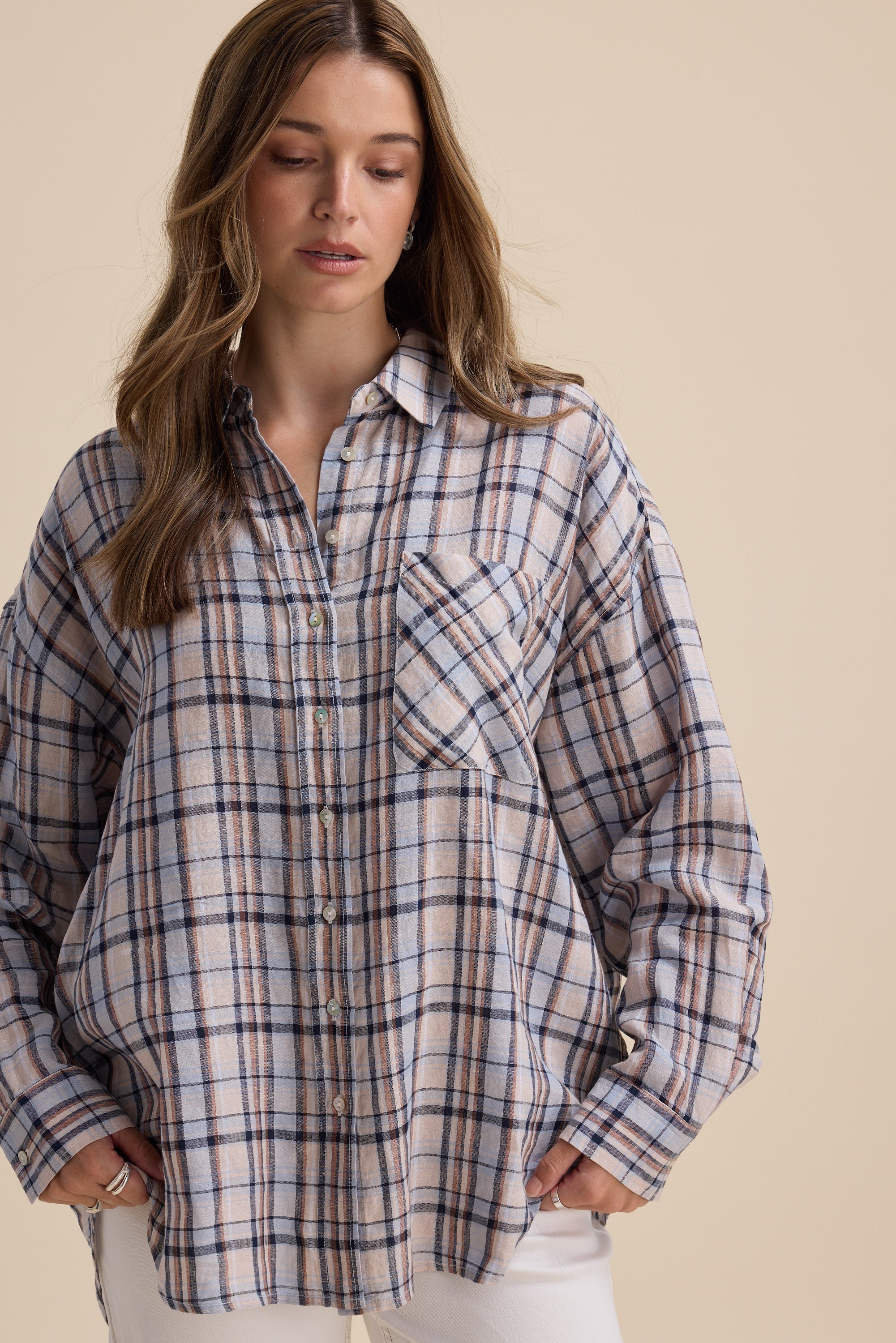 Woman wears the Elementary Oversized Shirt with hands in pockets, looking down.