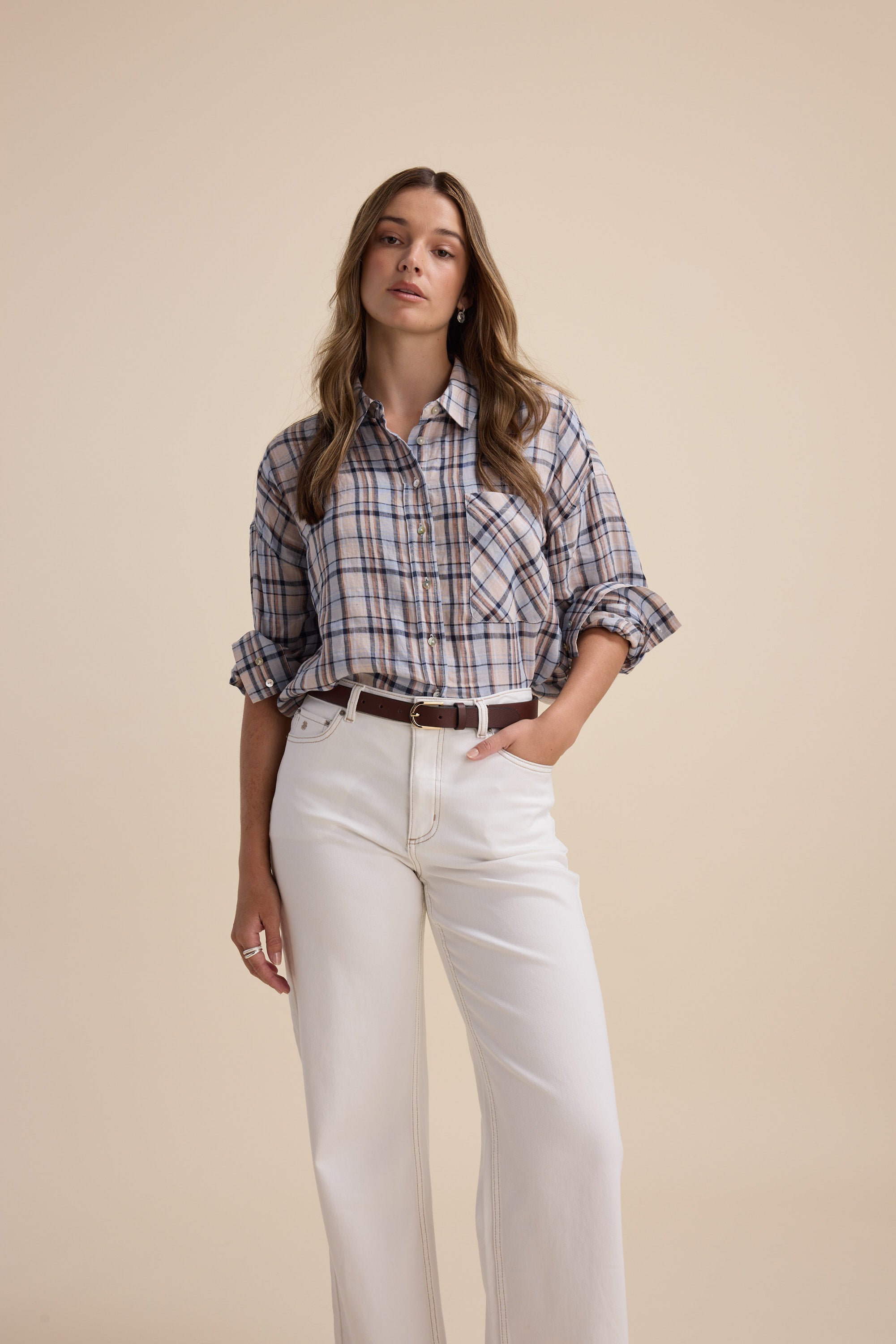 Woman wears Elementary Oversized Shirt with white pants against a beige background.