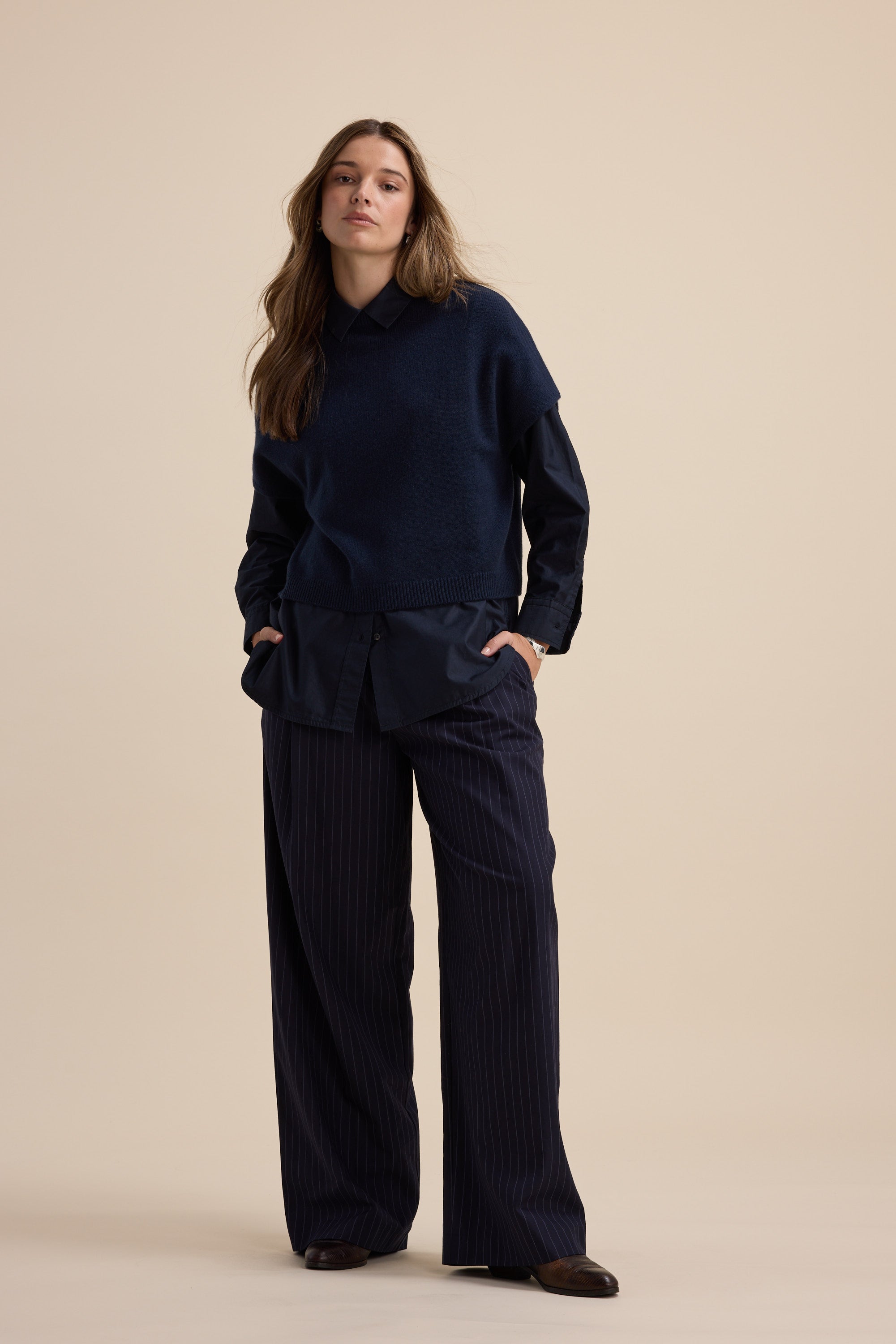 Woman in Elementary Cashmere Blend Drop Shoulder Top and pinstripe pants, navy on beige.