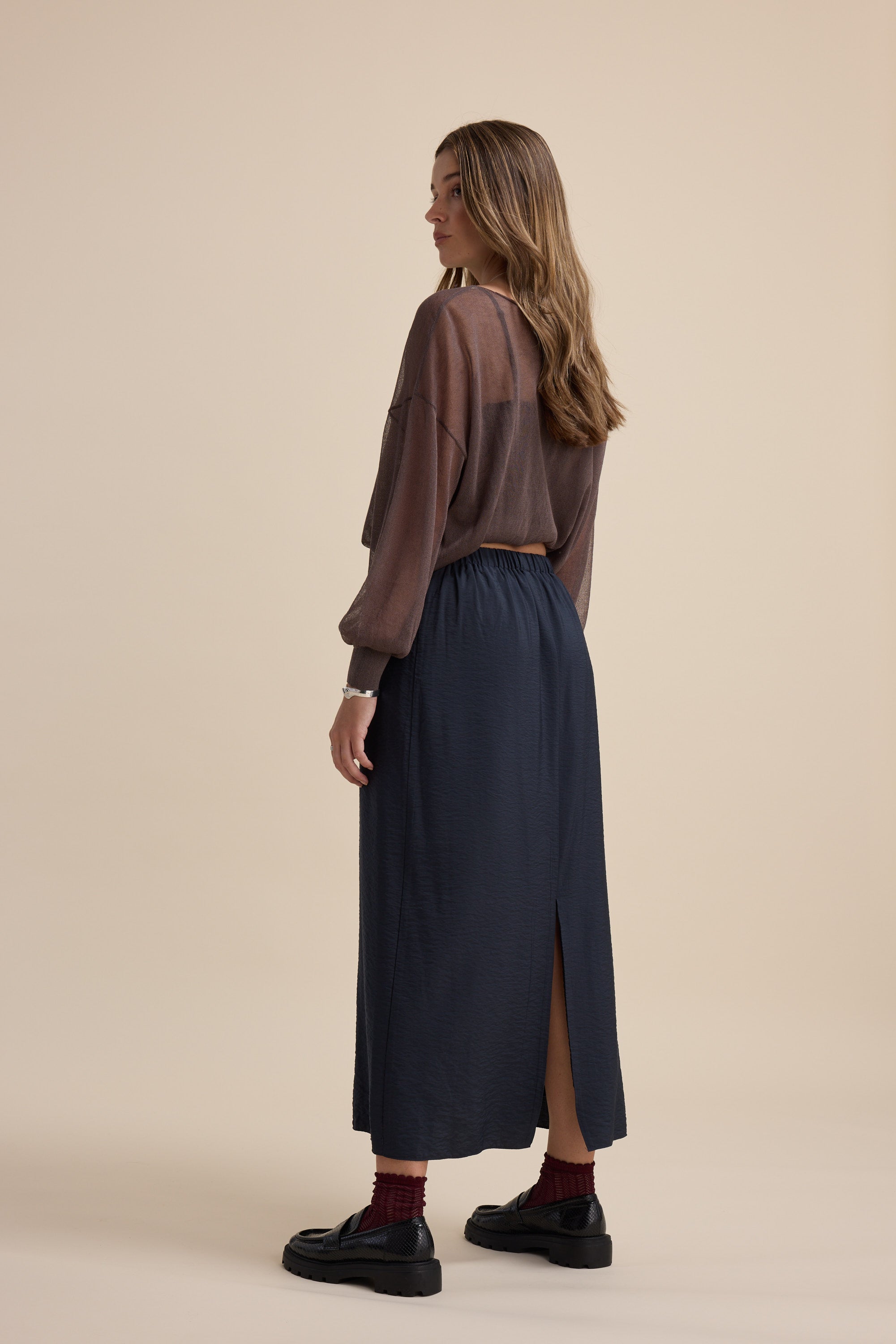 Woman in a brown top and Elementary's navy Wrap Detail Skirt, standing on a beige background.