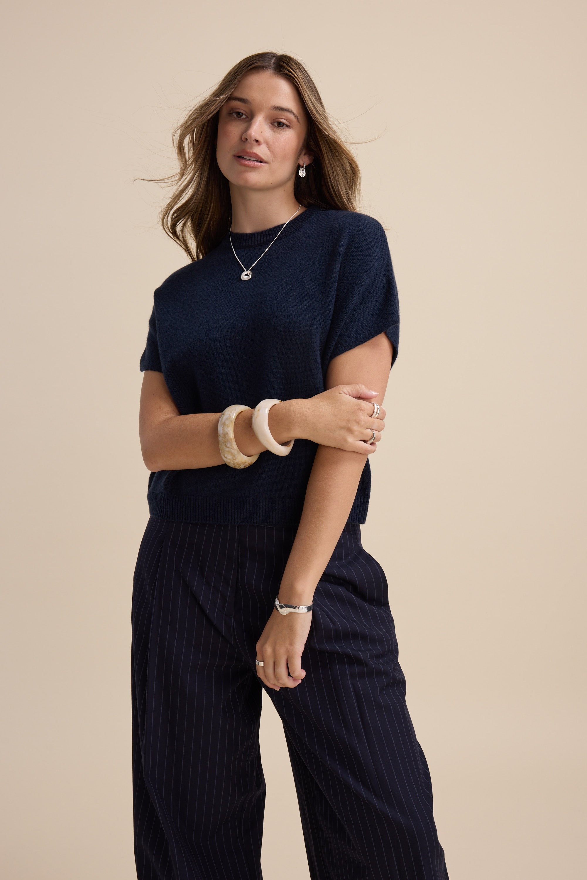 Woman in Elementary's cashmere blend drop shoulder top poses against a beige background.