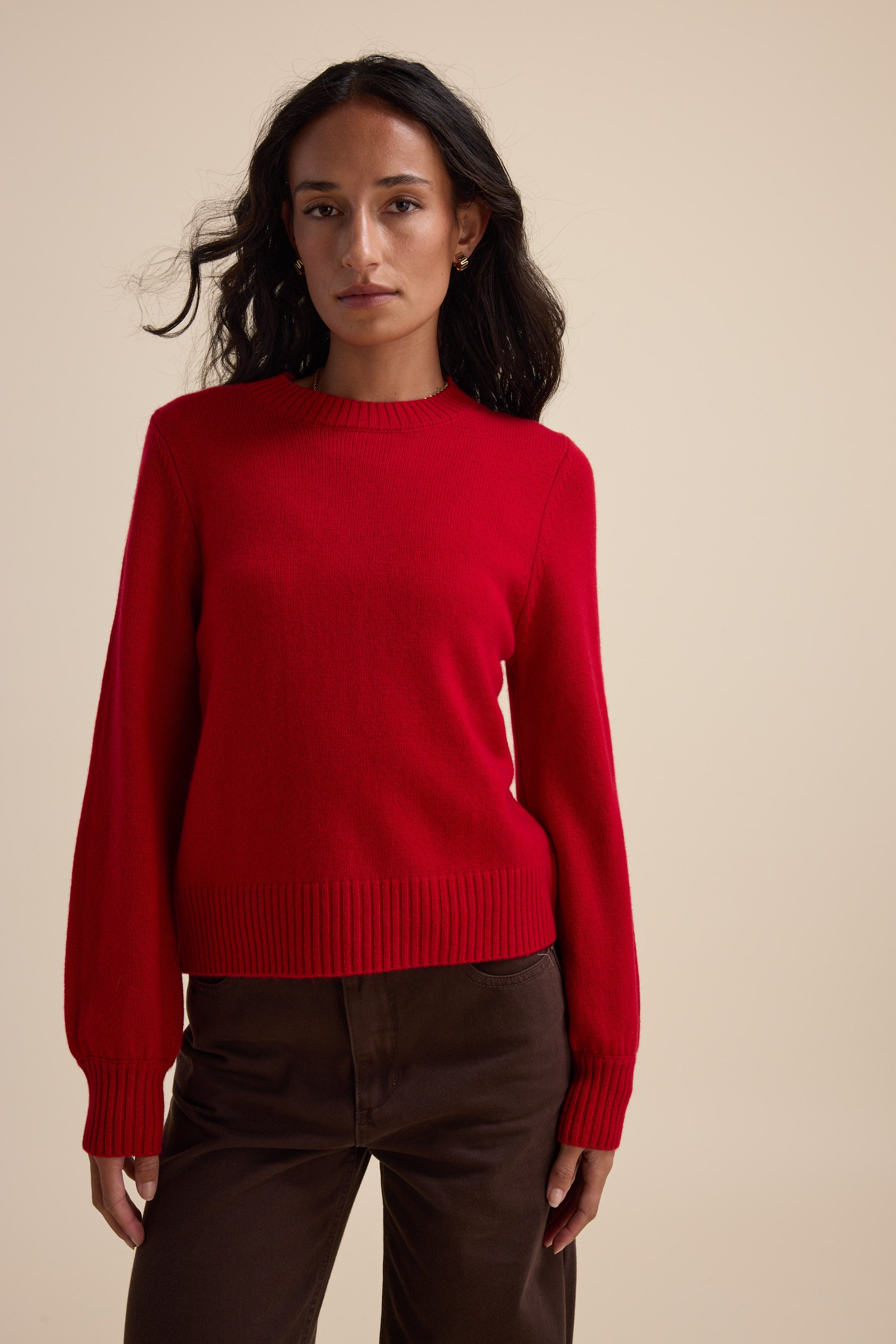 Woman in an Elementary Cashmere Blend Crew Neck Sweater and brown pants on a beige background.