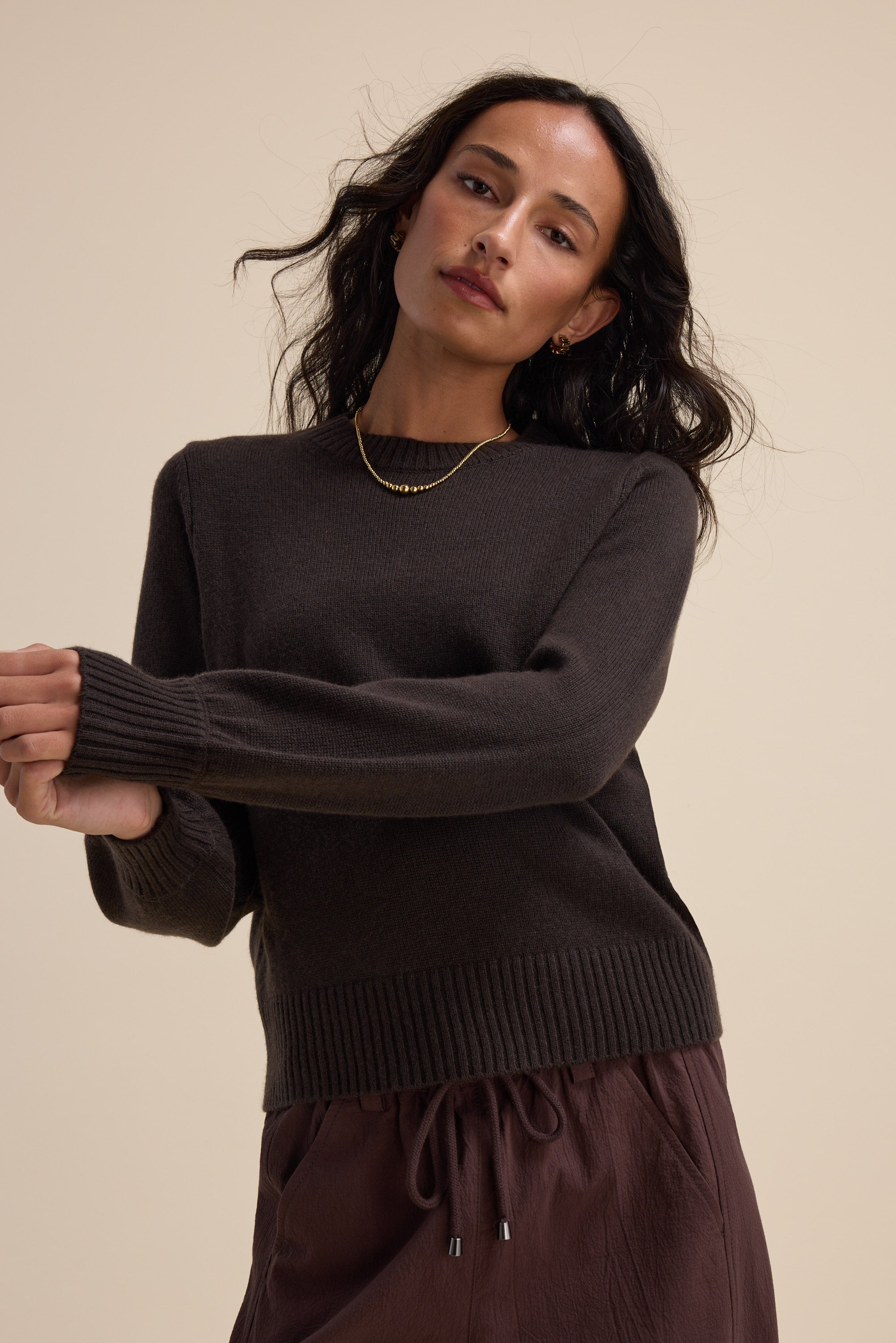 Woman in Elementary Cashmere Blend Crew Neck Sweater, arms raised against beige background.